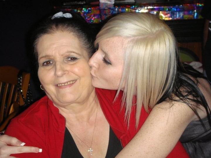 A young woman kisses her grandmother during a festive family celebration, radiating happiness.