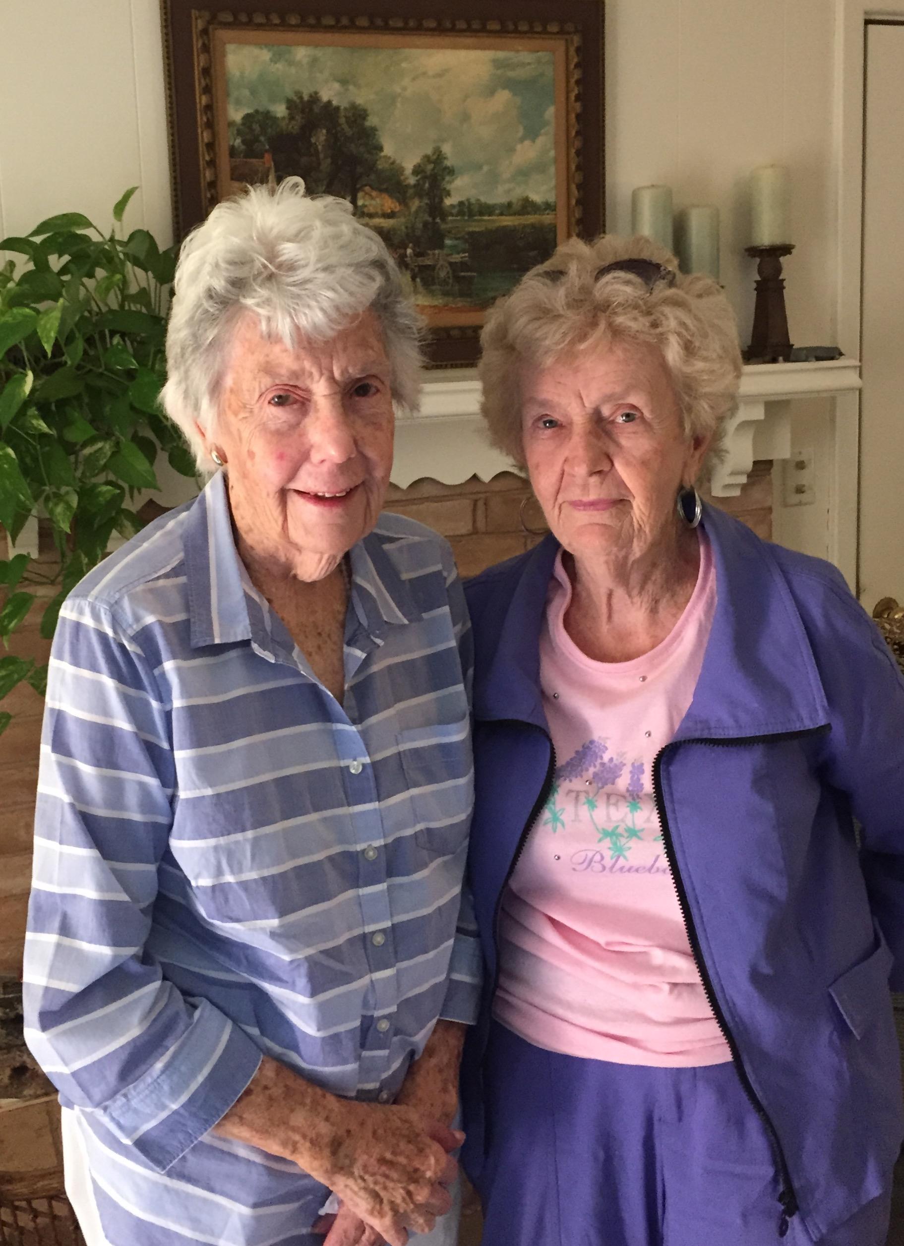 Two seniors pose happily in a comfortable living room, enjoying each other's company.