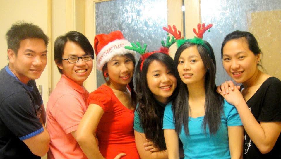 Four friends in holiday hats and antlers celebrate together indoors.