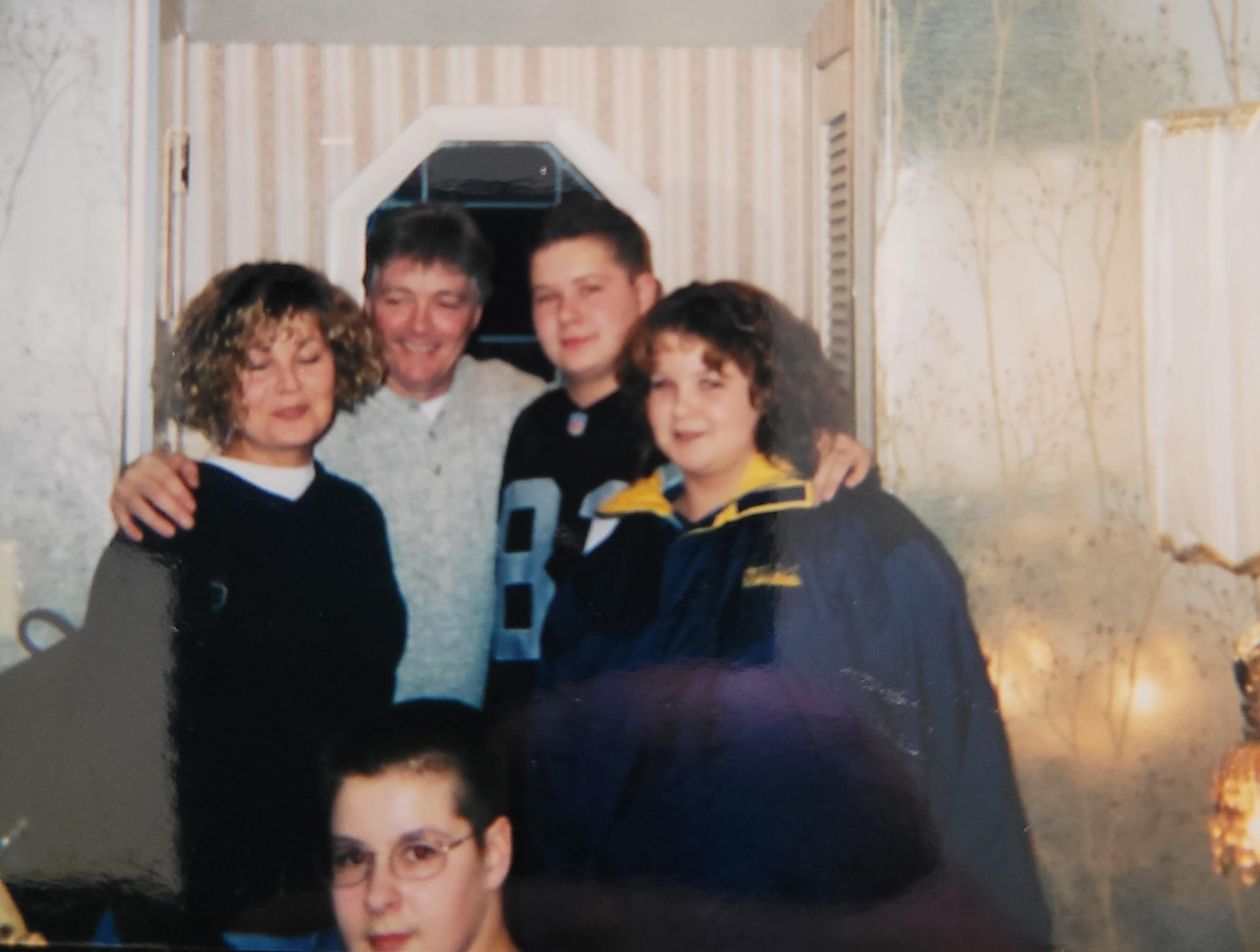 Group of five family members pose together, smiling in a cozy living room with soft lighting.