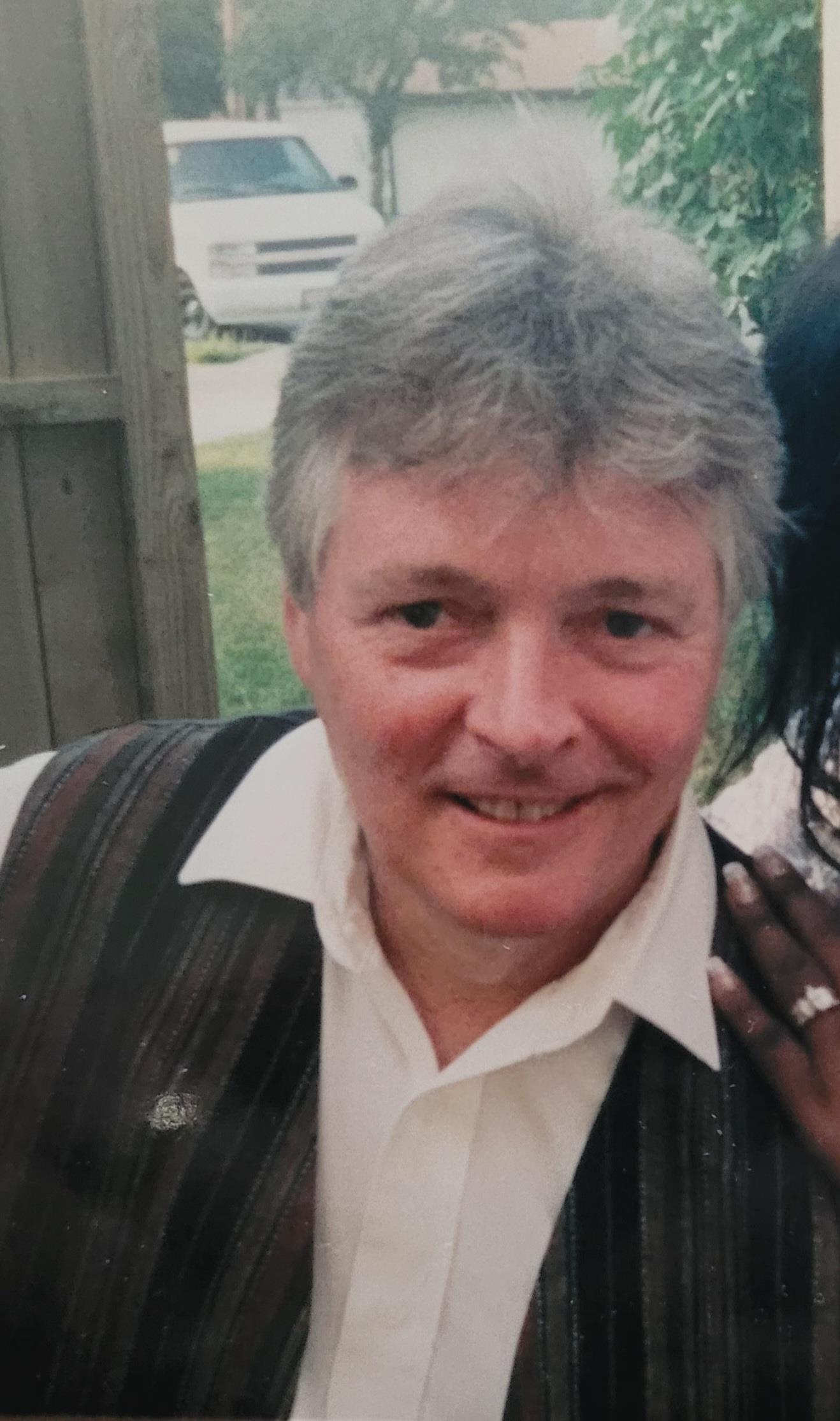 A cheerful man poses for a friendly photo with a woman at a gathering in bright sunshine.