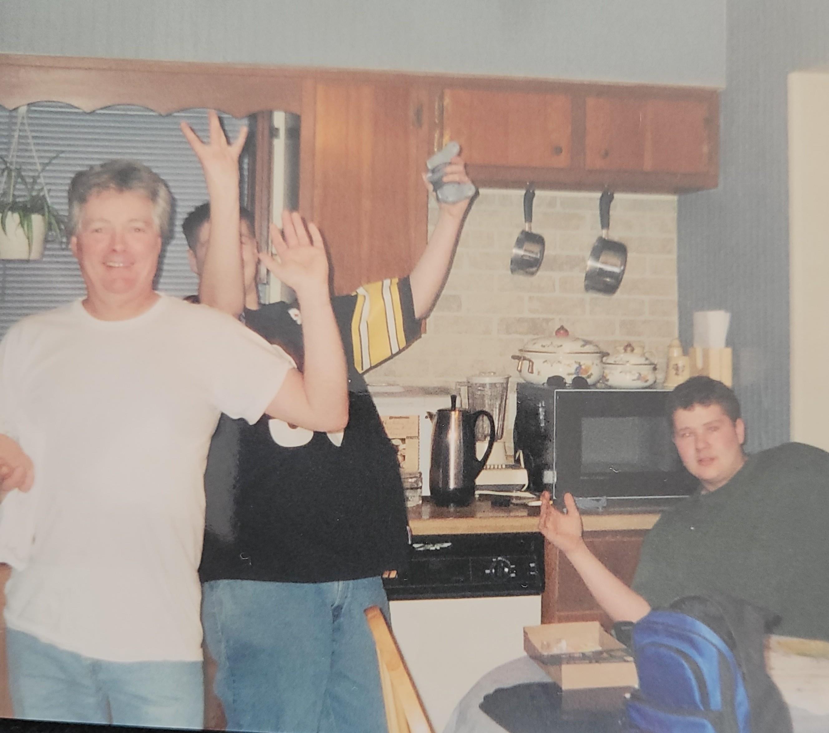 Four friends enjoy a lively moment in a kitchen, raising their hands and having fun together.