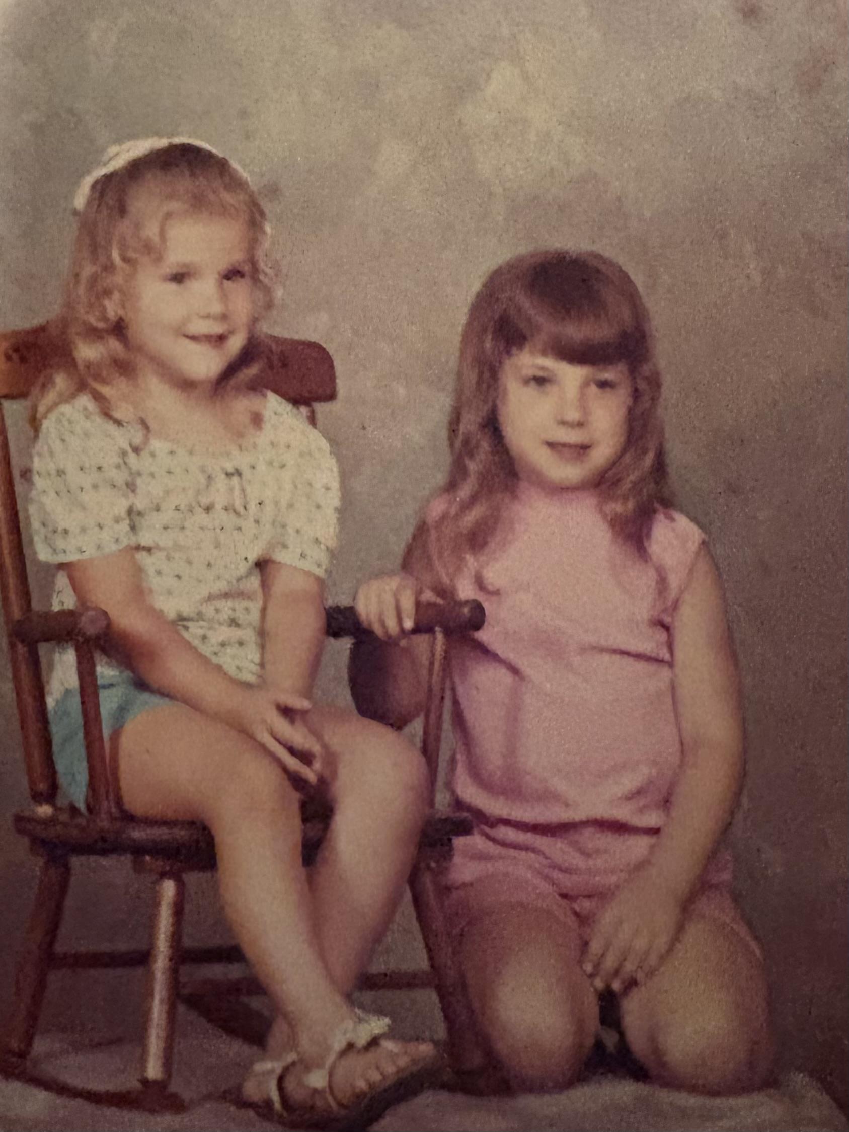 Two girls pose on a chair, displaying playful expressions in a nostalgic indoor environment.