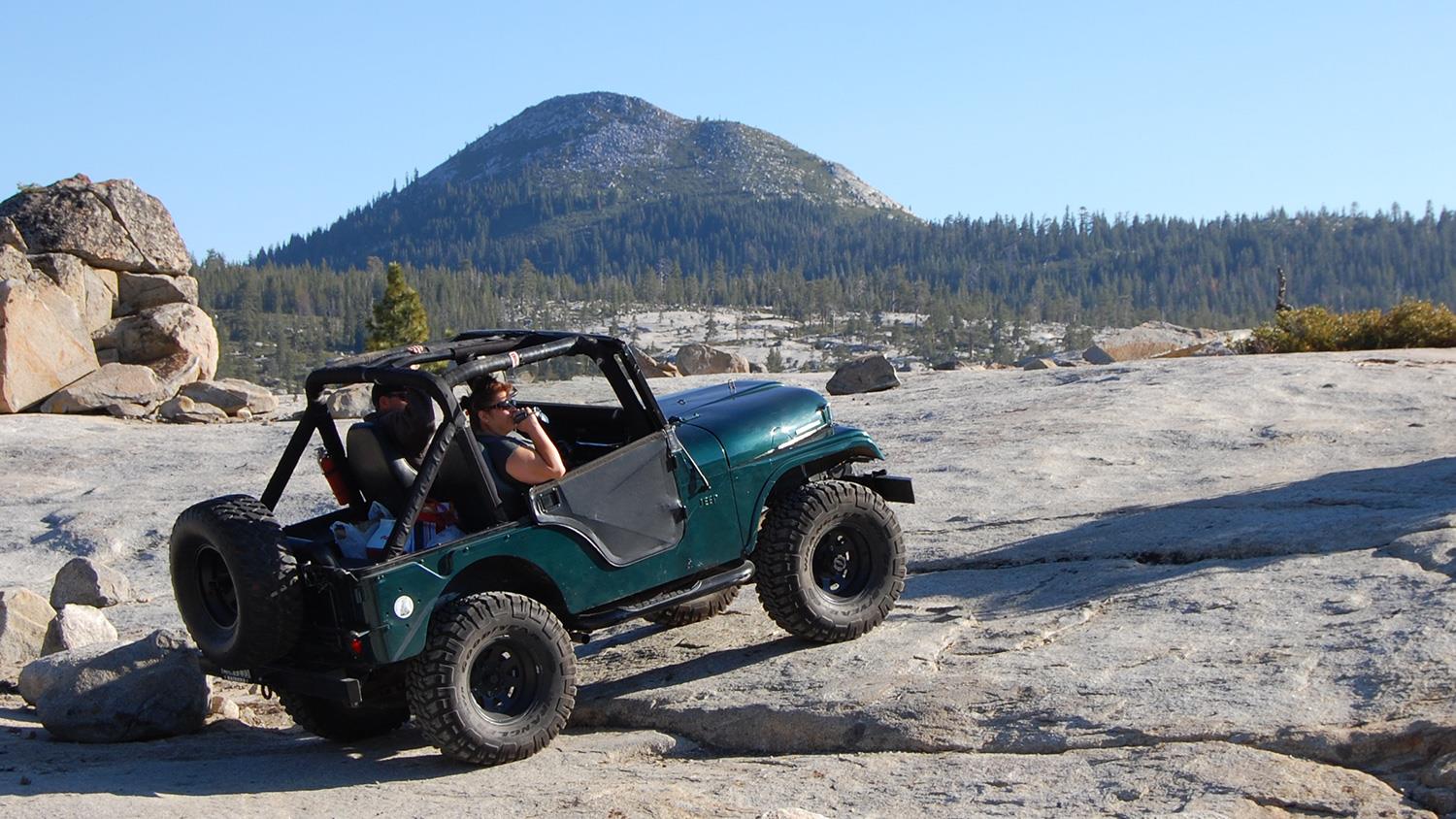A vintage off-road vehicle navigates rocky terrain with a driver enjoying the exhilarating outdoors.