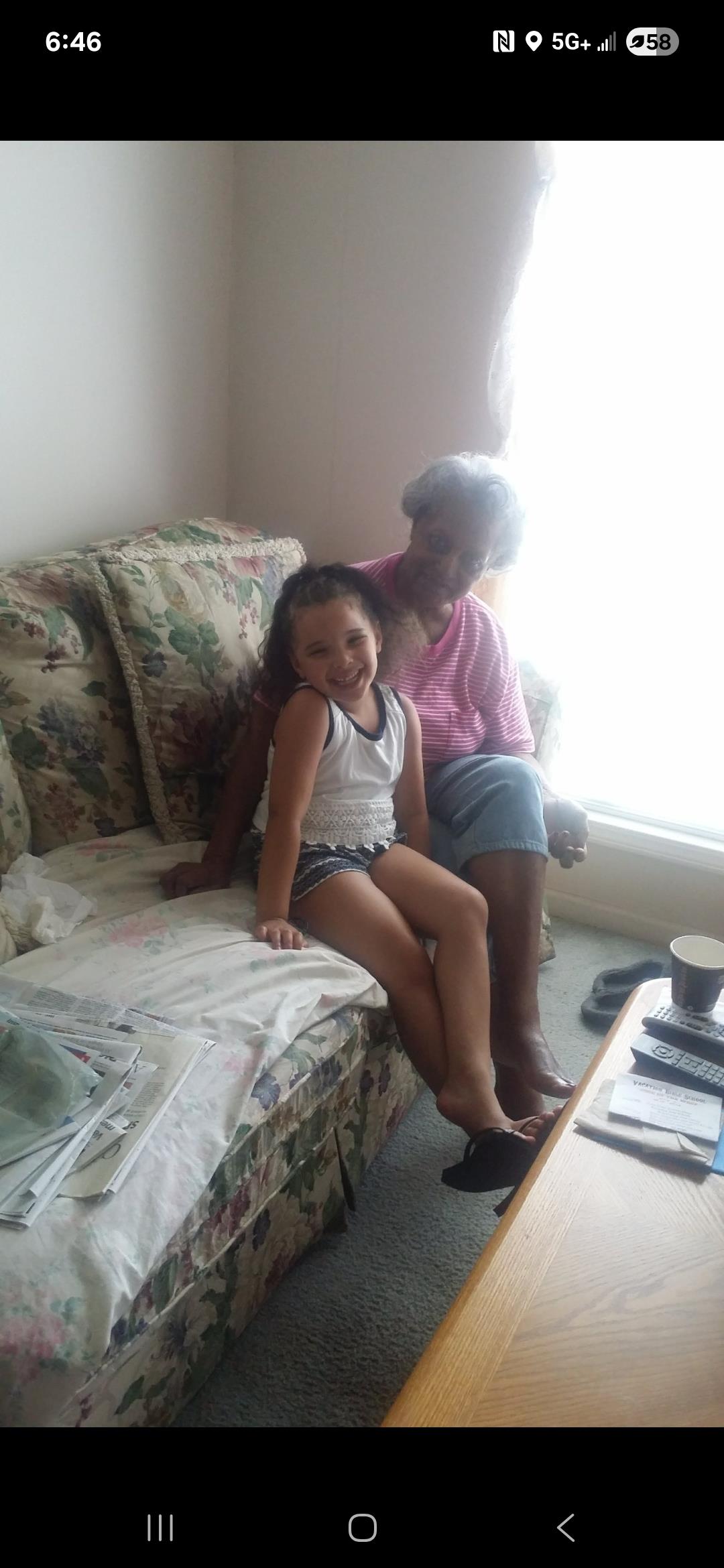 A young girl sits beside her grandmother, both smiling joyfully and enjoying the bright moment.