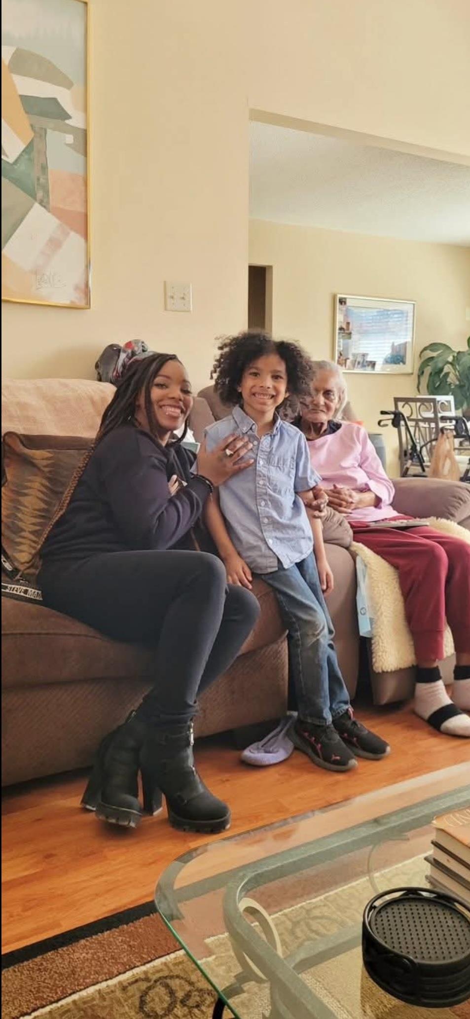 Three family members share smiles and laughter while sitting on a couch at home.