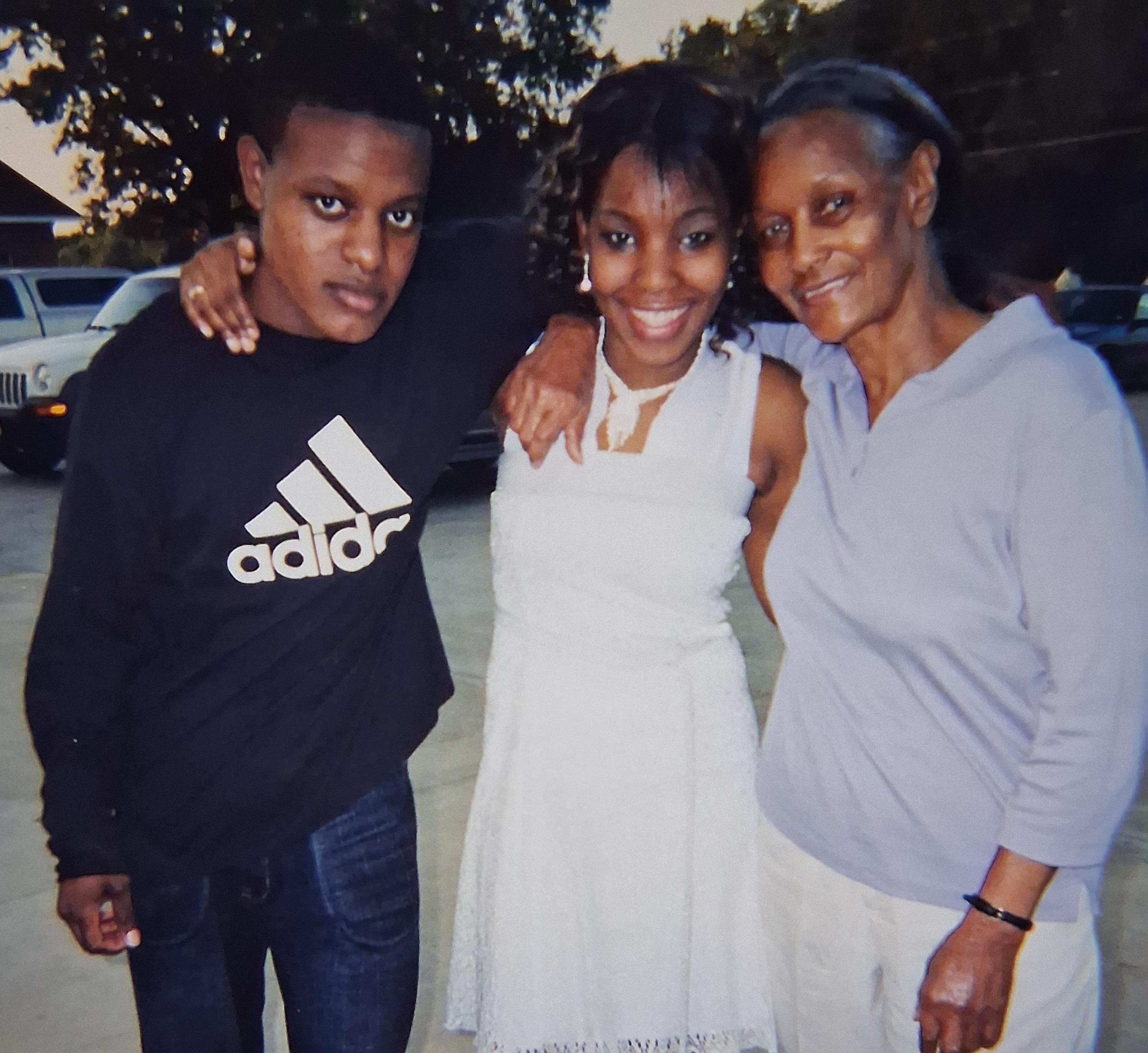 Two young adults and a woman smile while celebrating together in the park at dusk.