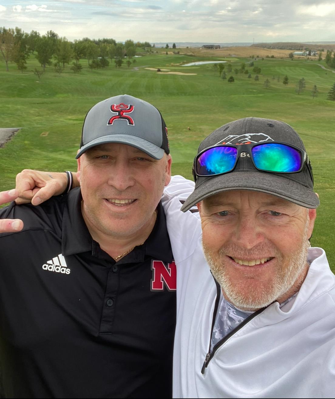 Two friends hug on the golf course, smiling under the sunny sky and enjoying their day.