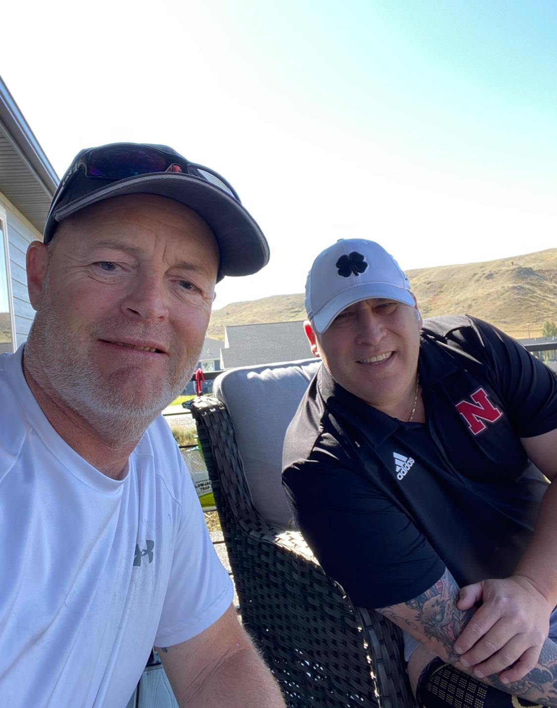 Two friends relax on a patio, smiling and enjoying the warm sunshine on a clear day.
