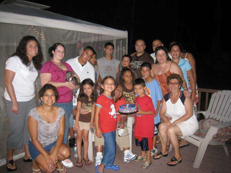 A joyful night celebration with kids holding a cake and happy adults smiling together.