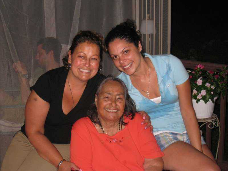 Three women smile together in a cozy indoor space, reflecting their family love.
