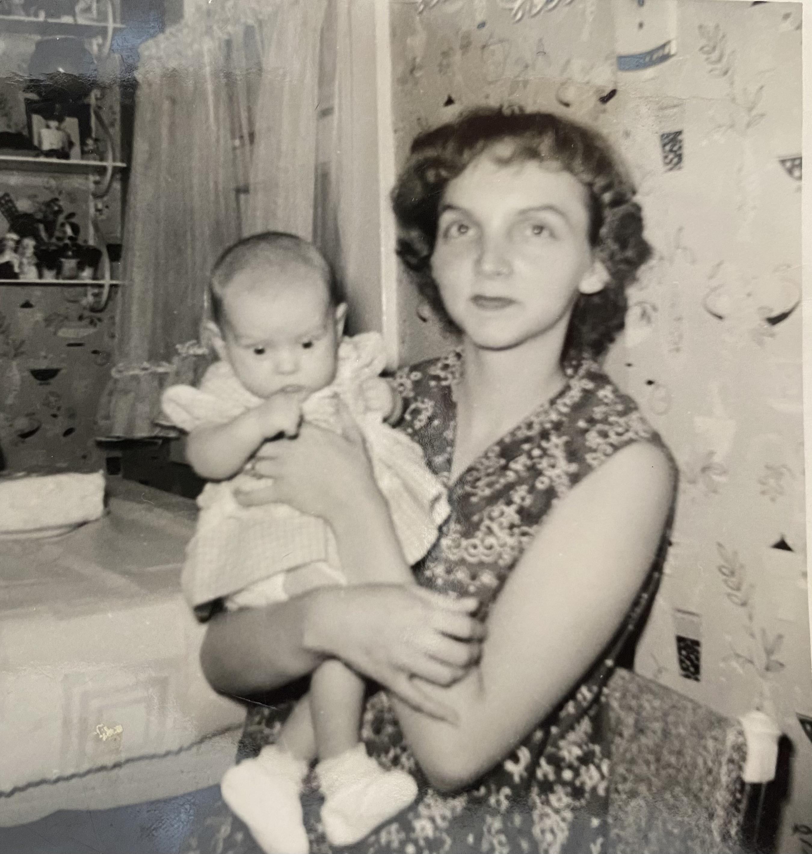 A mother holds her baby in a warm living space with vintage decor from the 1960s.