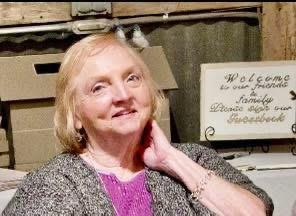 A cheerful older woman interacts with visitors at a vintage decor exhibition, exuding warmth.