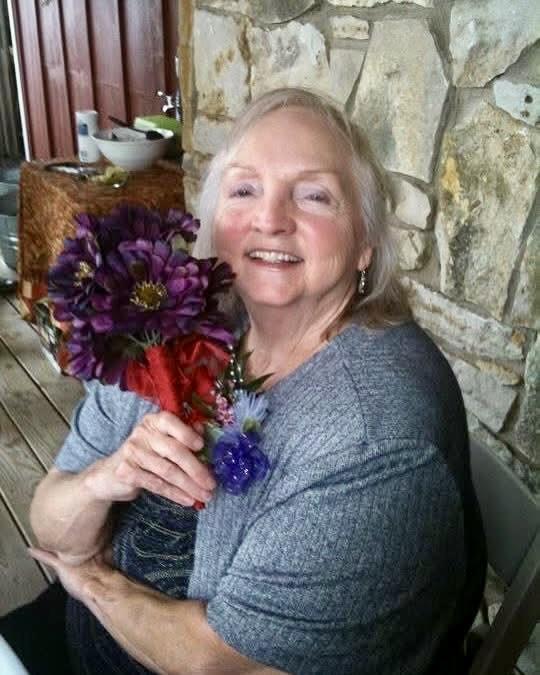 A cheerful woman is holding a bouquet of vibrant flowers while sitting on a porch.