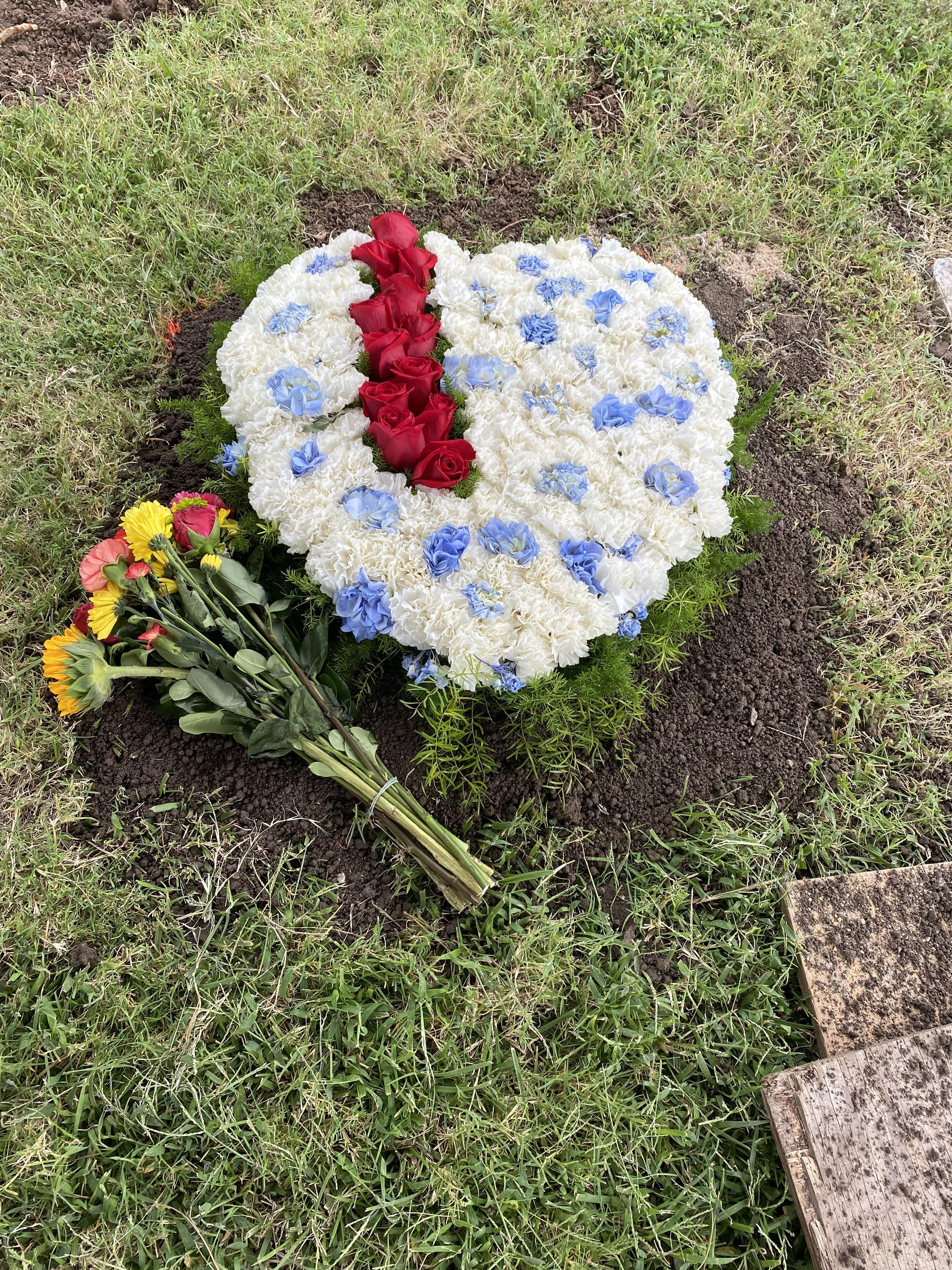 A heart-shaped floral tribute made of white, red, and blue flowers rests on the ground.