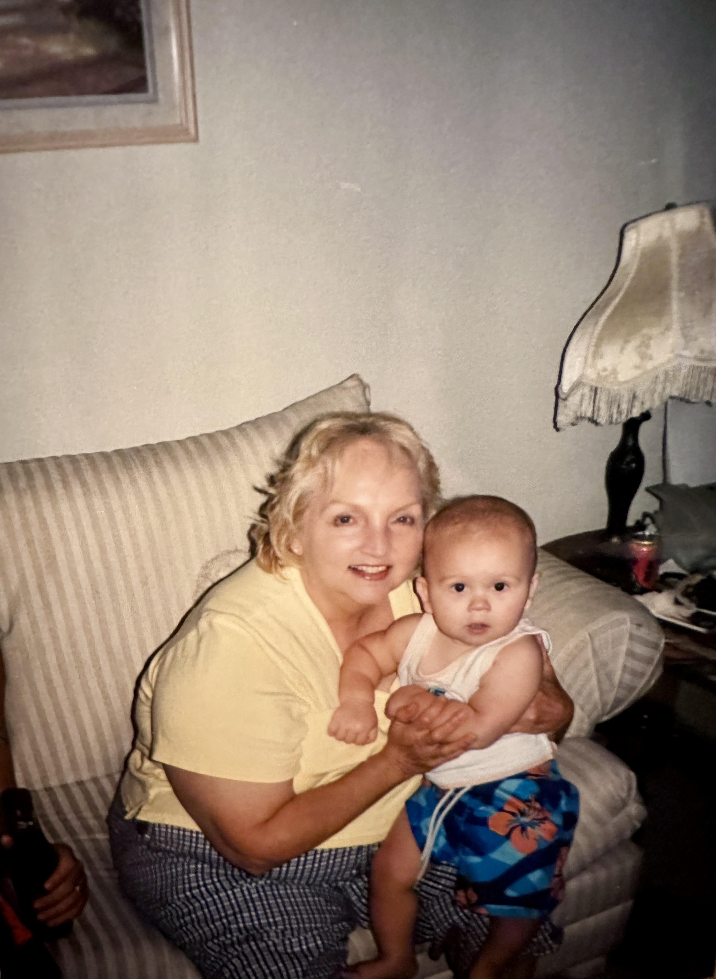 A cheerful elderly woman smiles while holding a baby in a cozy living room setting.