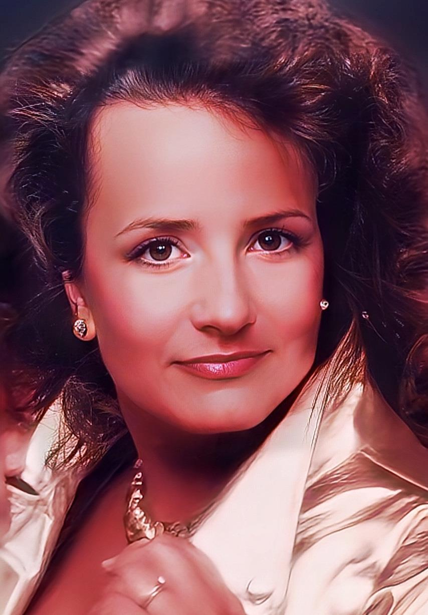 A confident woman with curly hair, blazer, and jewelry gazes directly at the camera.