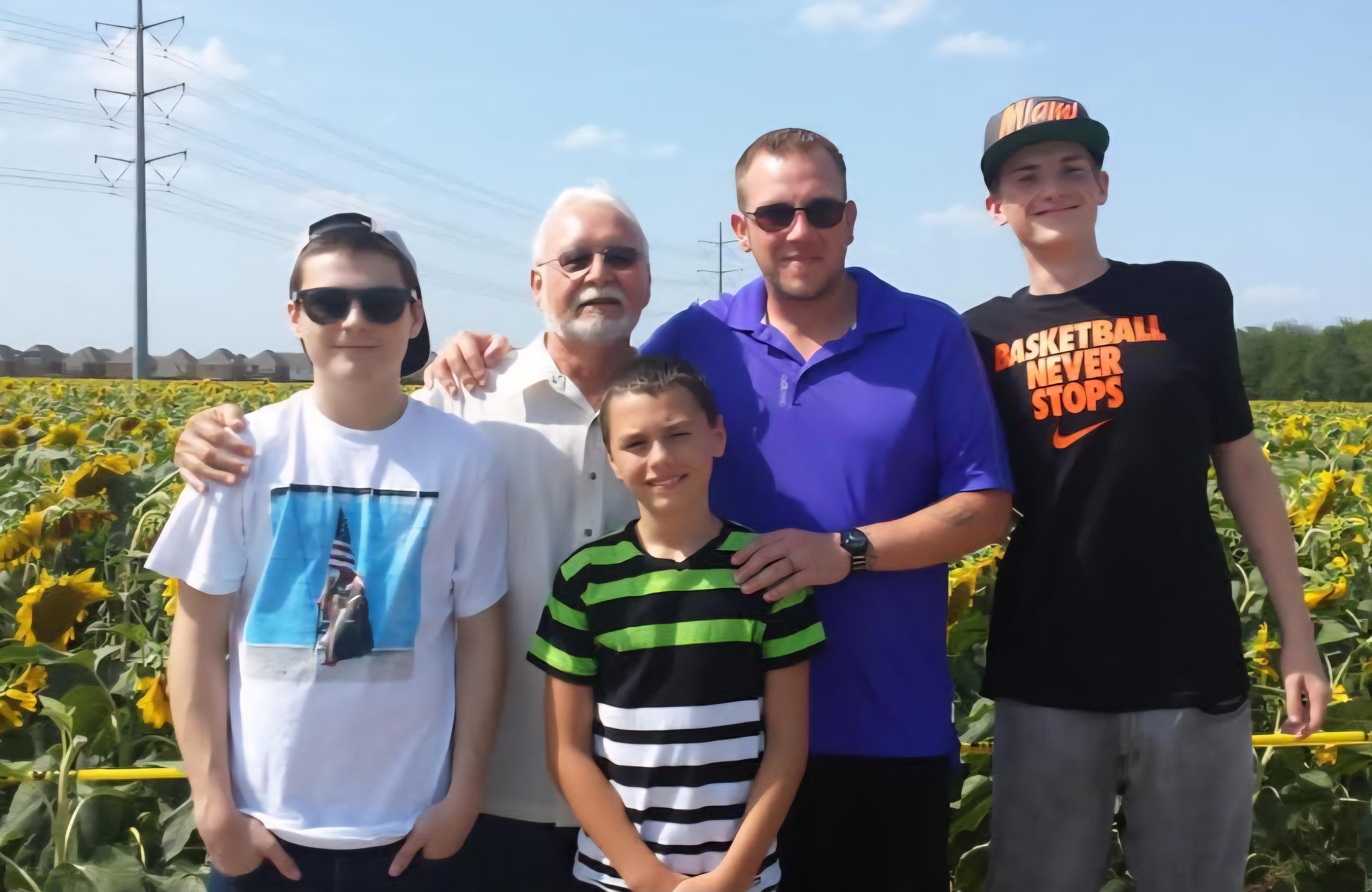 Five family members pose for a cheerful photo outdoors, enjoying a bright, sunny day.