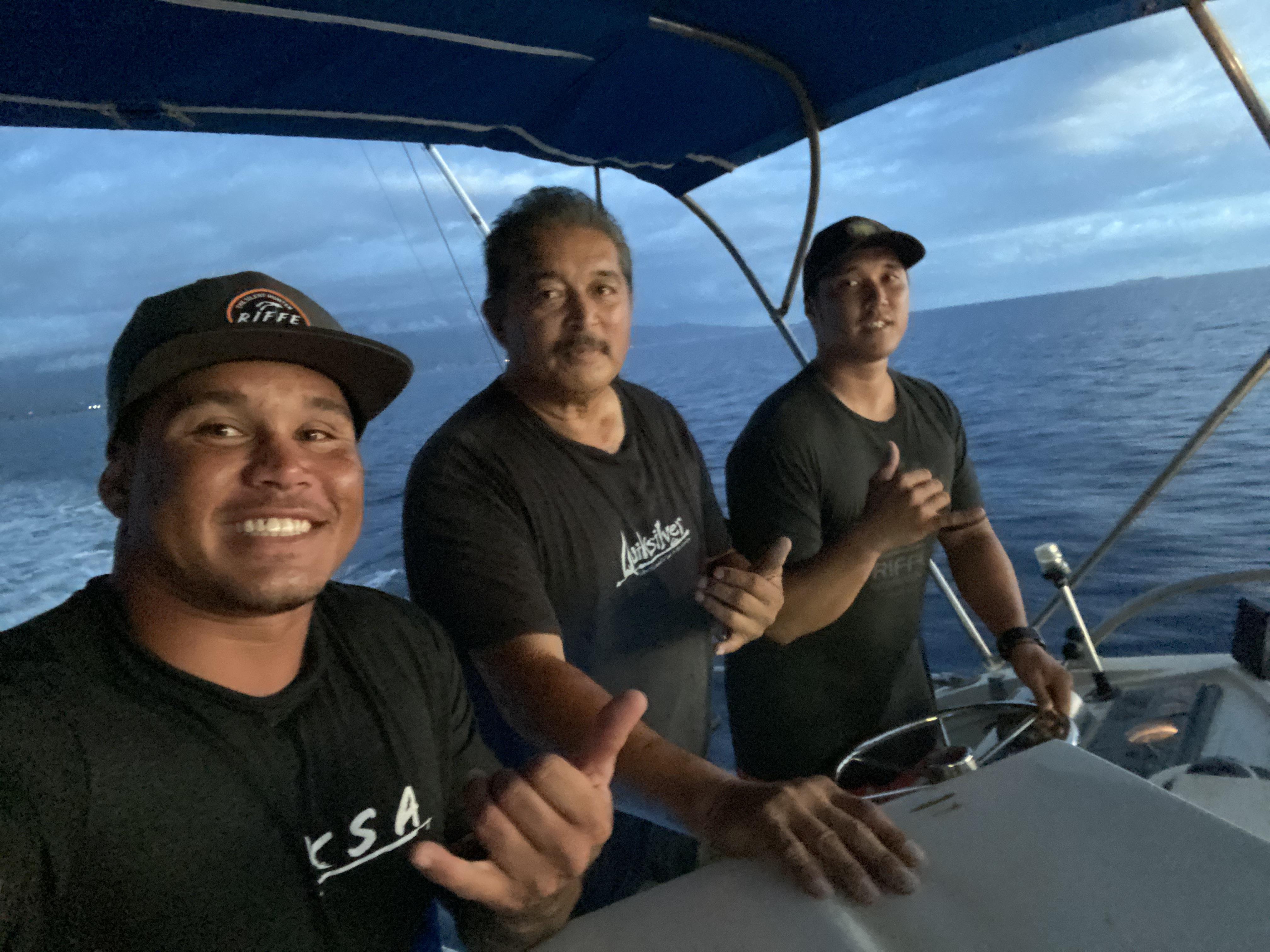 Three friends smile on a boat, surrounded by calm ocean waters at sunset.