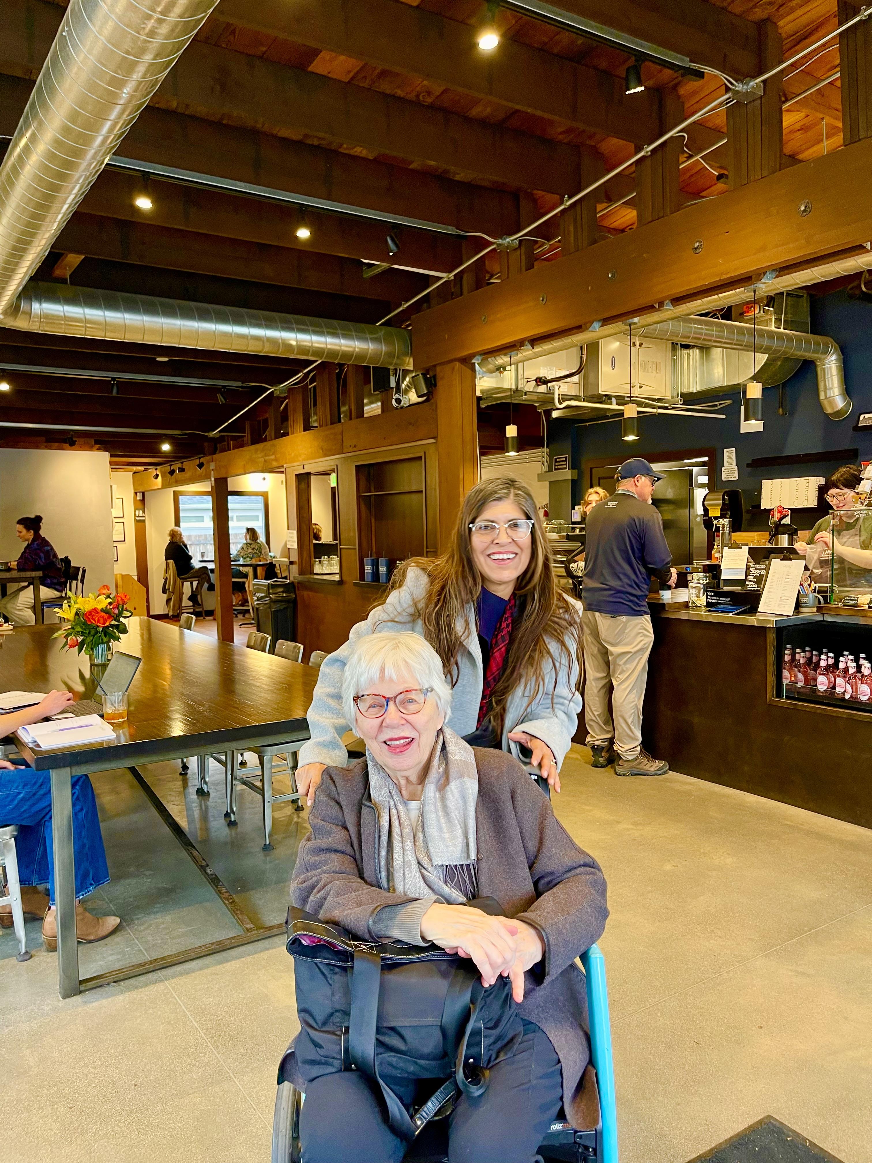Two friends share a moment of joy in a lively cafe, surrounded by people and vibrant decor.
