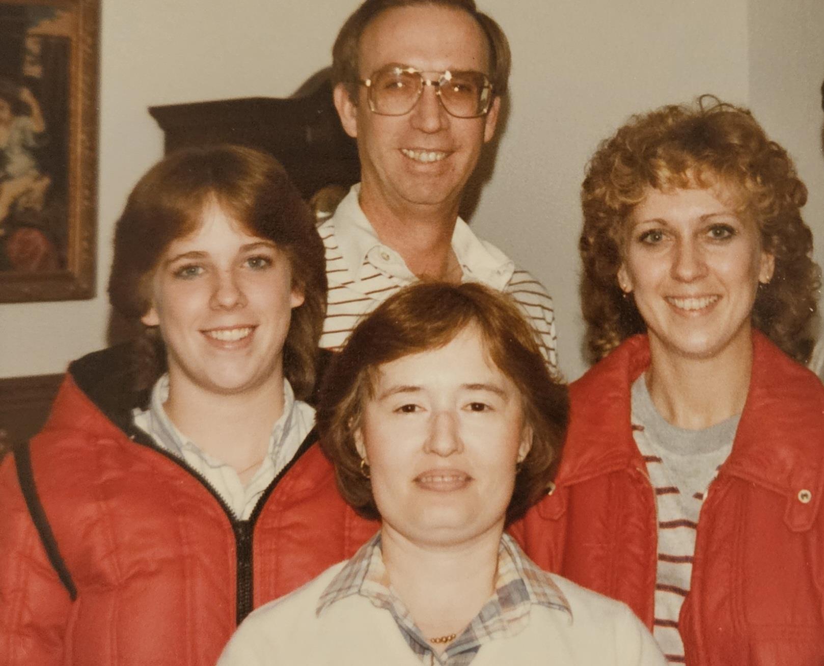 Four people in matching jackets smile together in a cozy indoor setting.