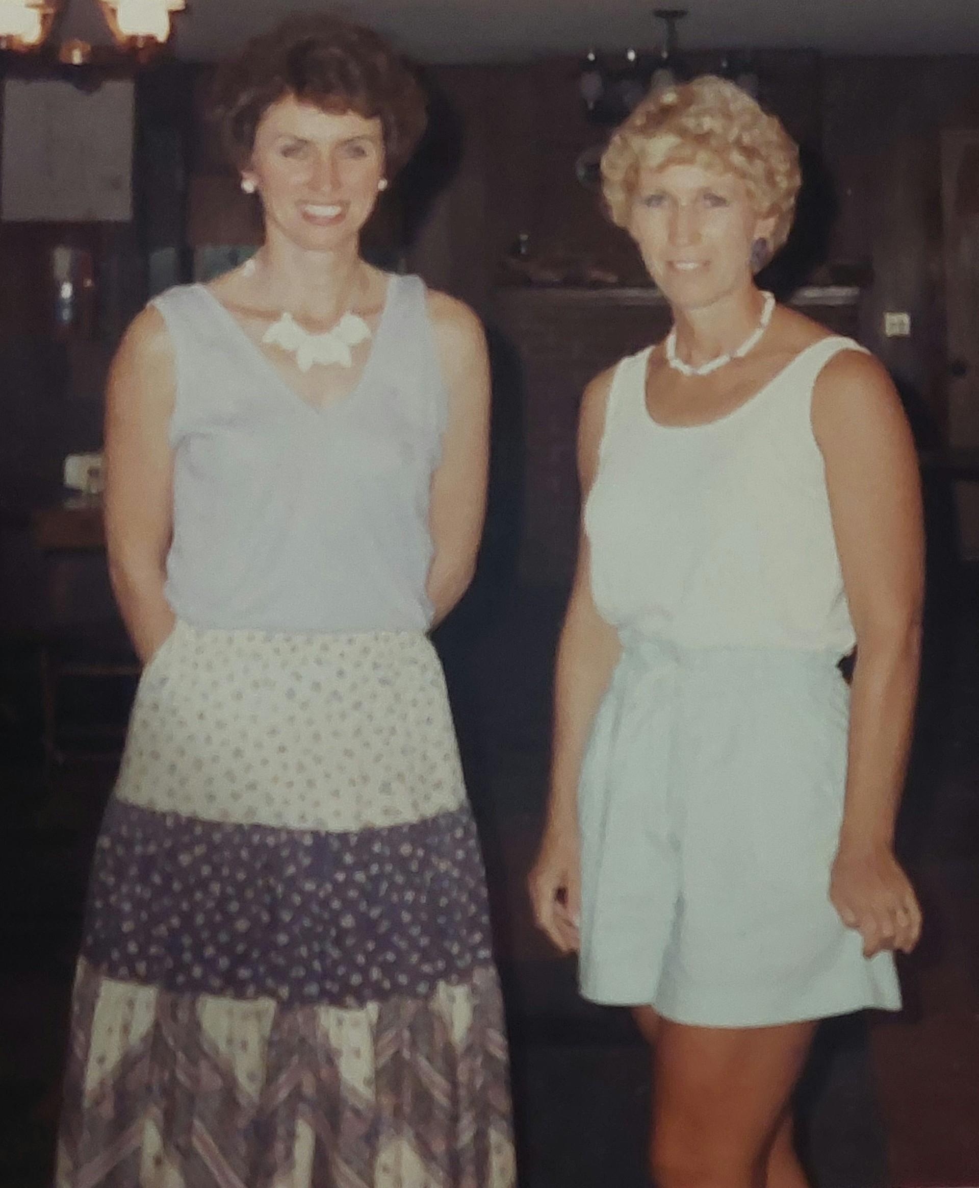 Two women stand side by side, smiling, showcasing their vintage summer attire from the 1960s.