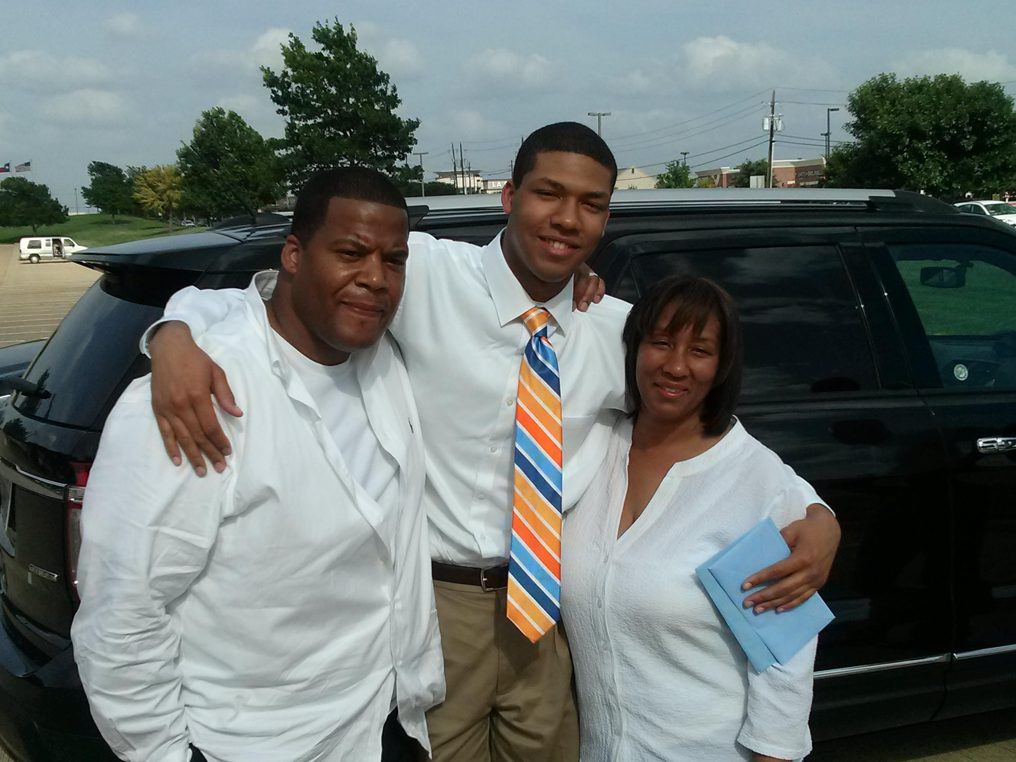 Family smiles together in white outfits and a striped tie, celebrating outdoors.