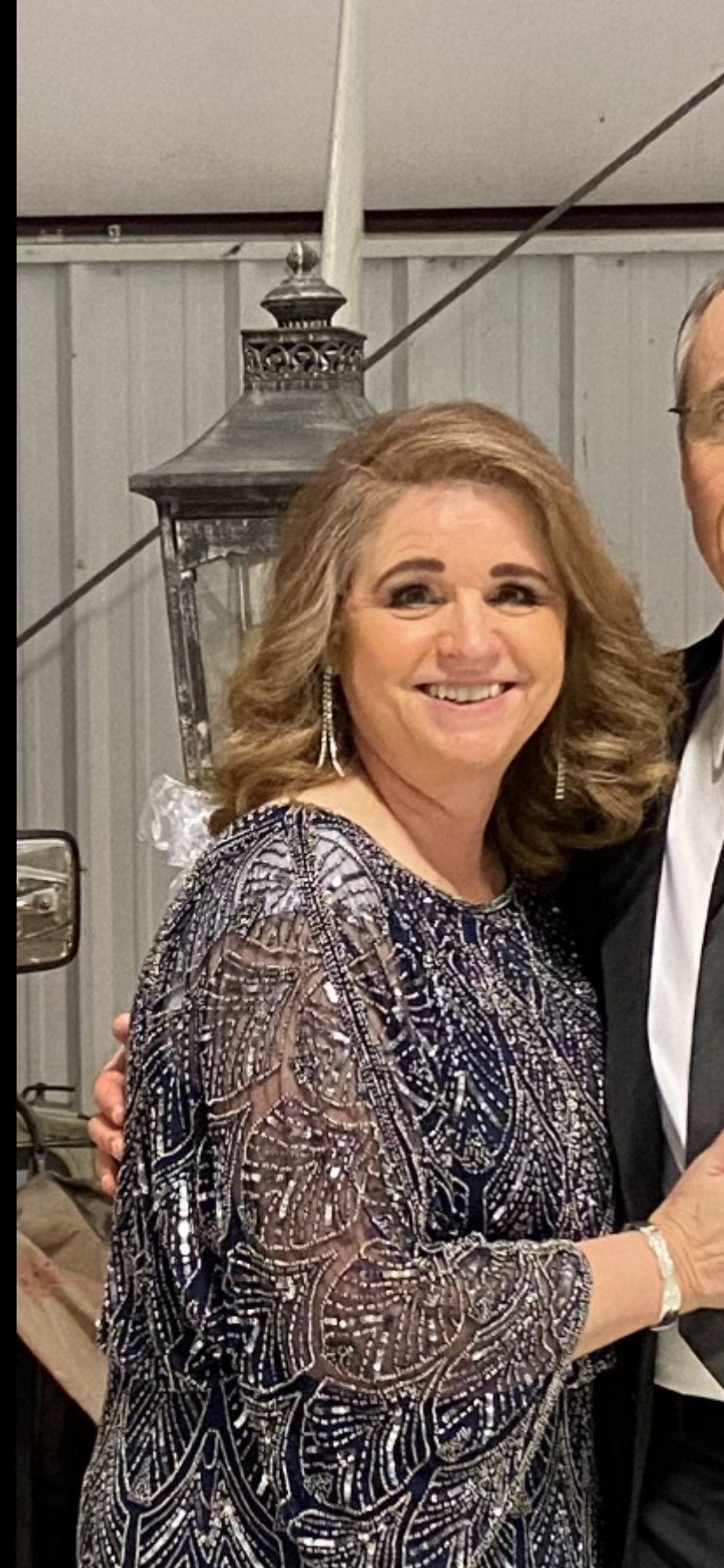 A woman wearing a glittery dress smiles warmly at the camera during an outdoor evening gathering.