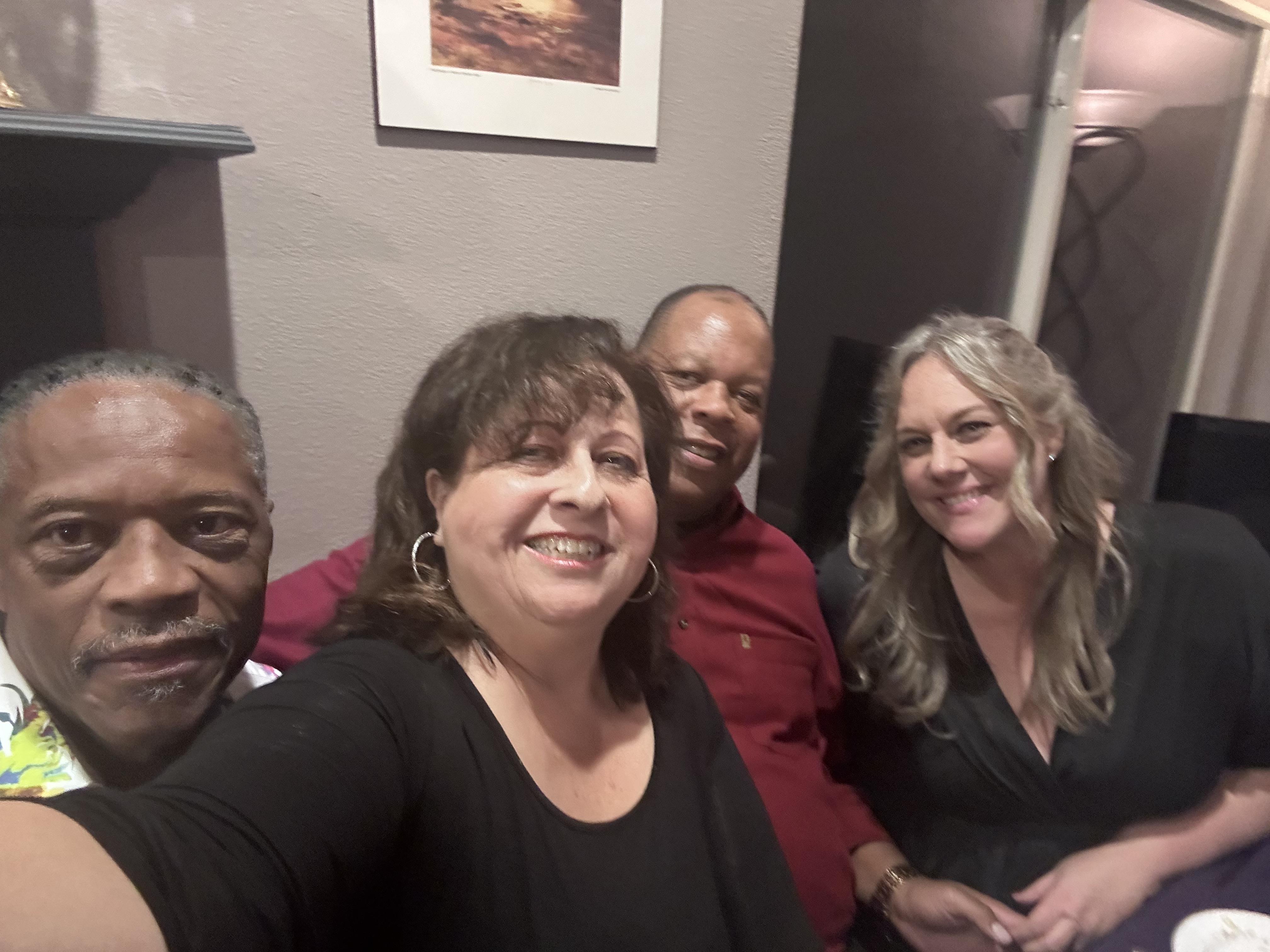 Four friends smile together in a cozy room, enjoying each other's company on a fun night out.