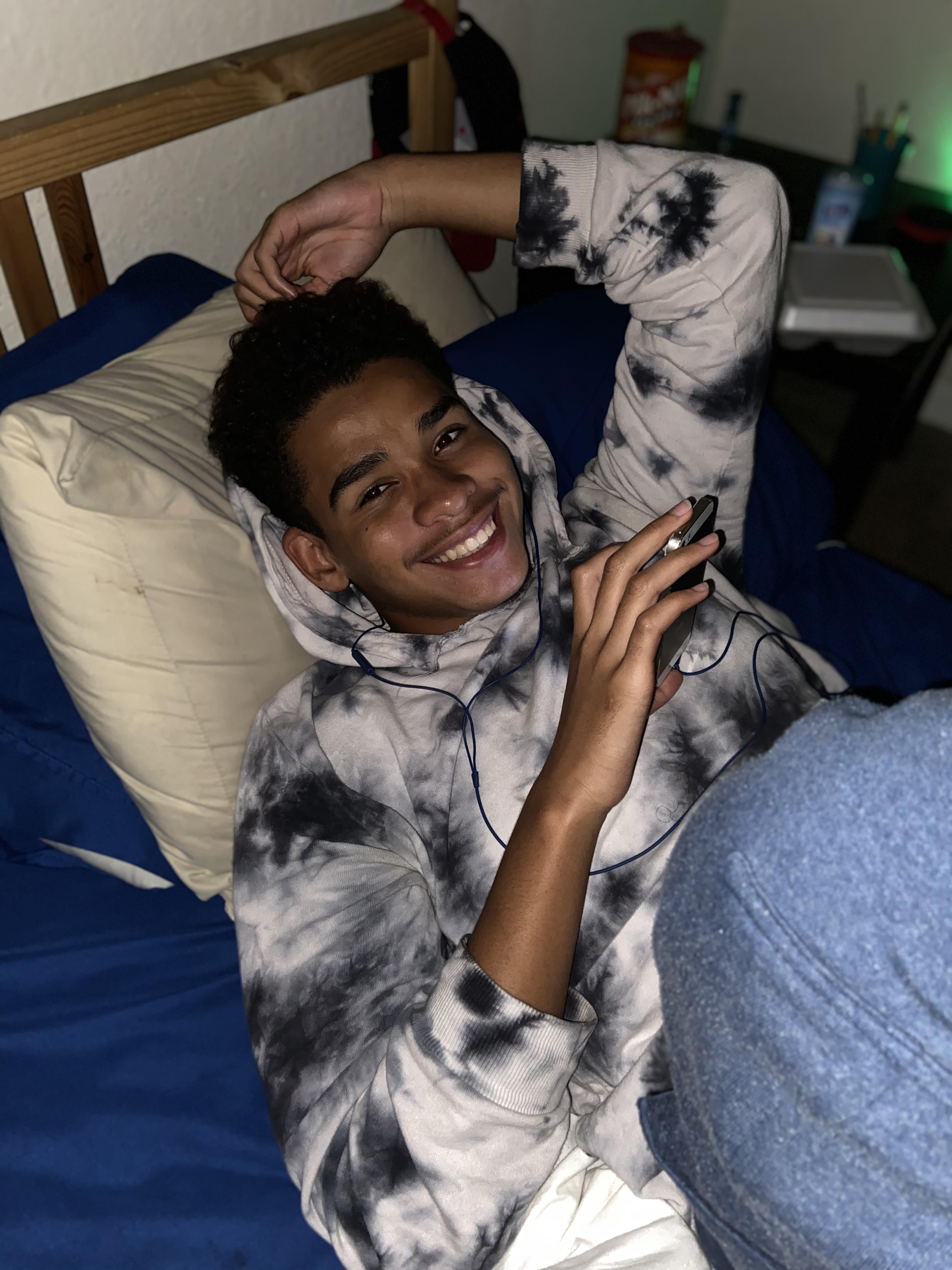 A man lying on a bed with his hand up and a phone