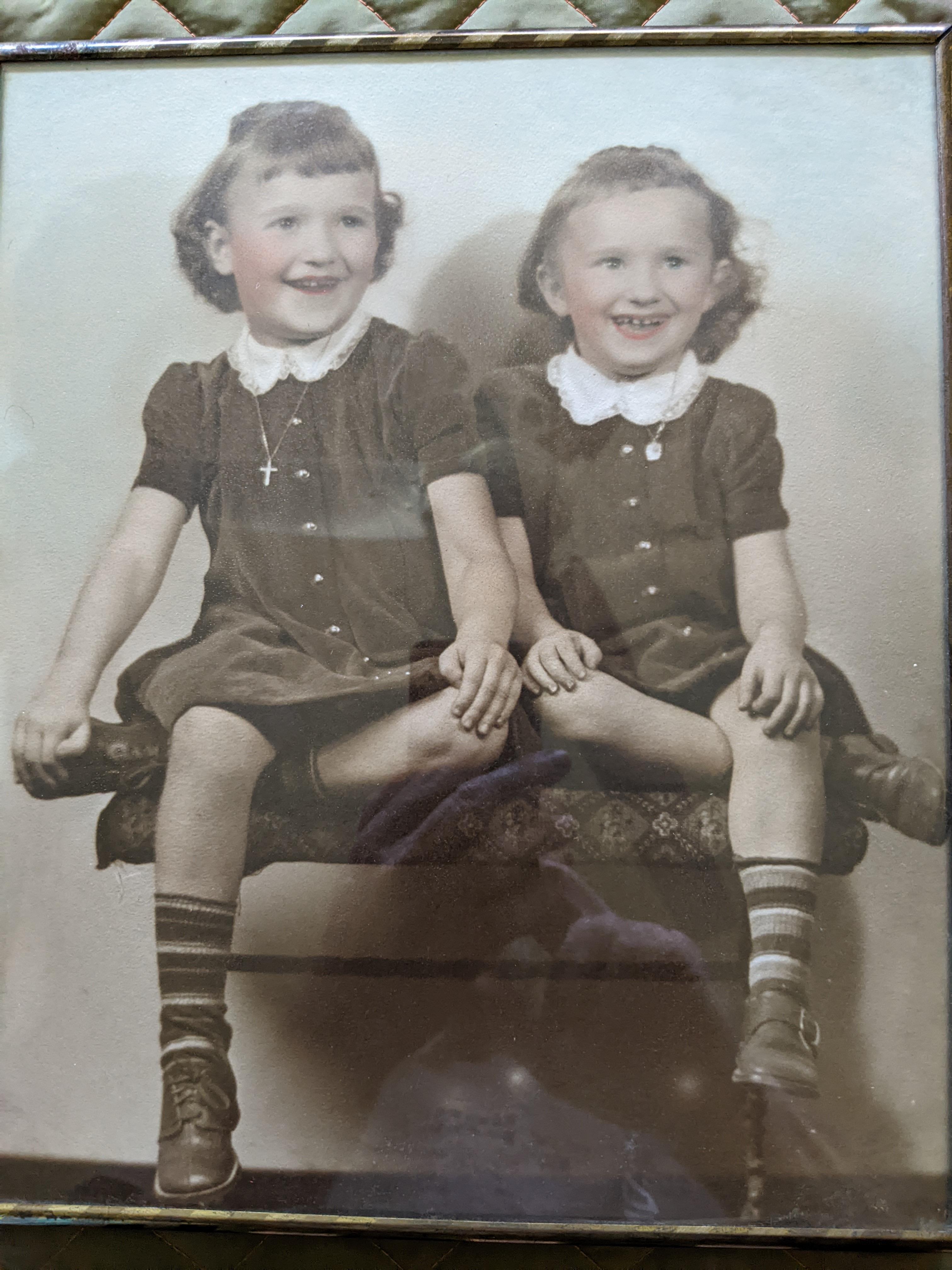 Two cheerful young sisters dressed in identical outfits sit together on a bench, sharing a moment.