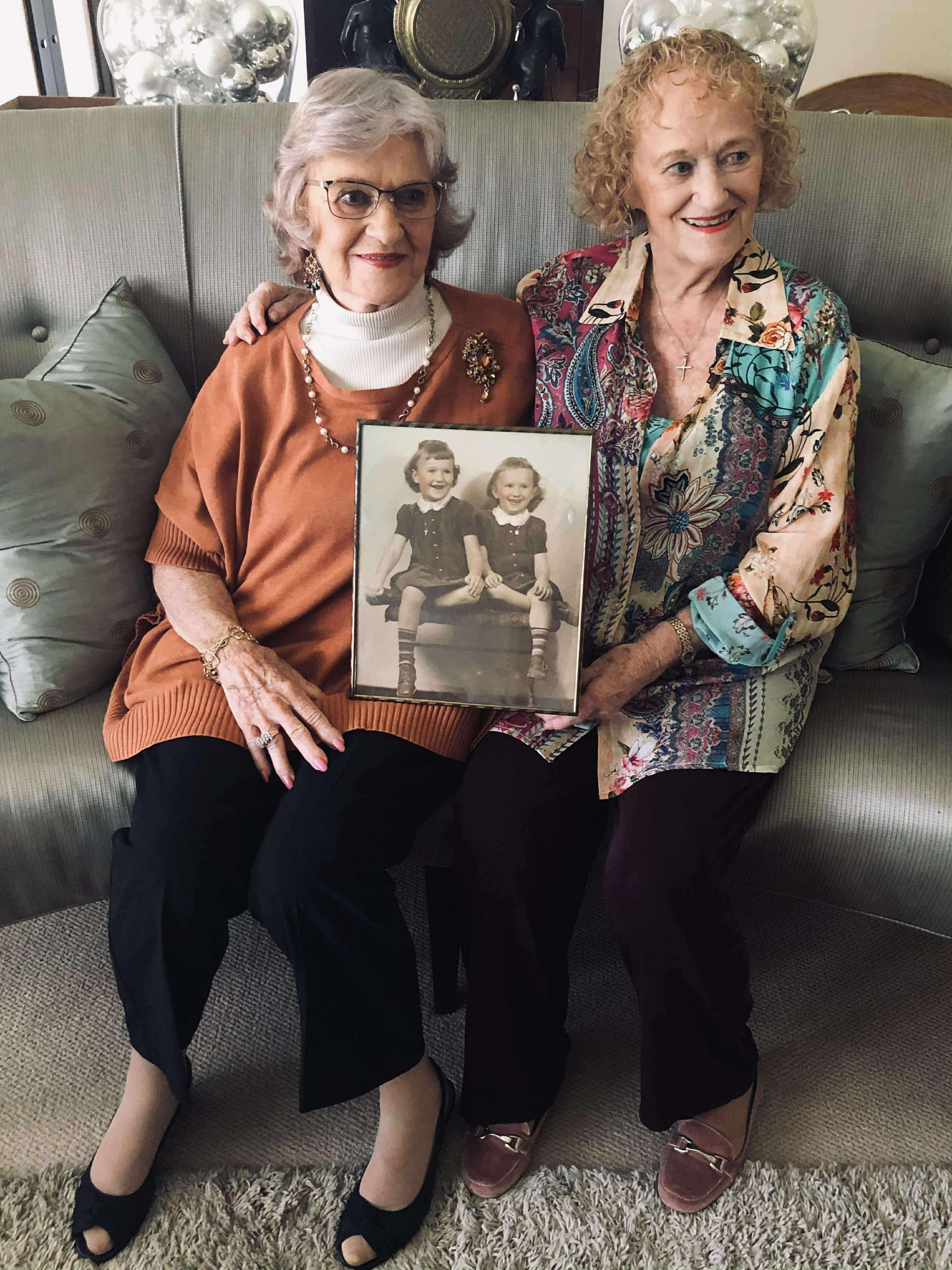Two women proudly showcase a vintage photograph of their childhood, smiling warmly.