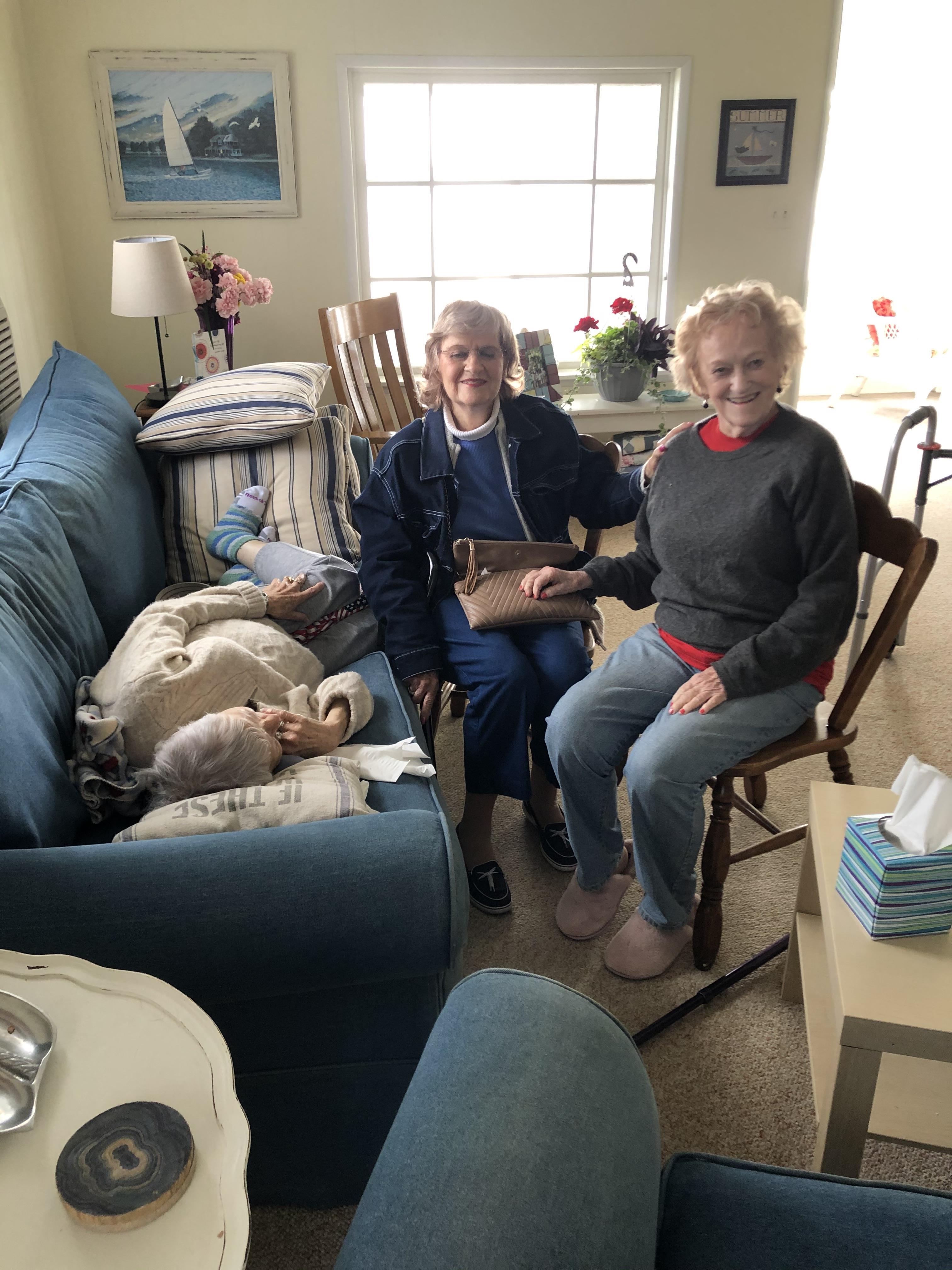 Three elderly women share a joyful moment on a comfortable couch while engaging in conversation.
