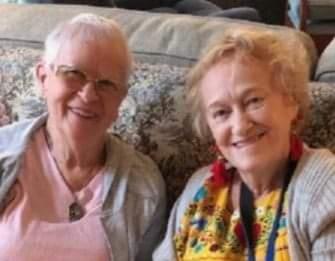Two smiling women sit together in a comfortable room, sharing a warm and happy moment.