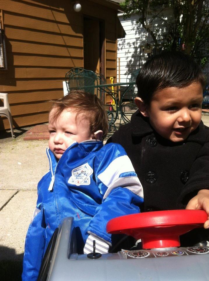 Two young children enjoy riding a toy vehicle in a sunny backyard, showcasing friendship and fun.