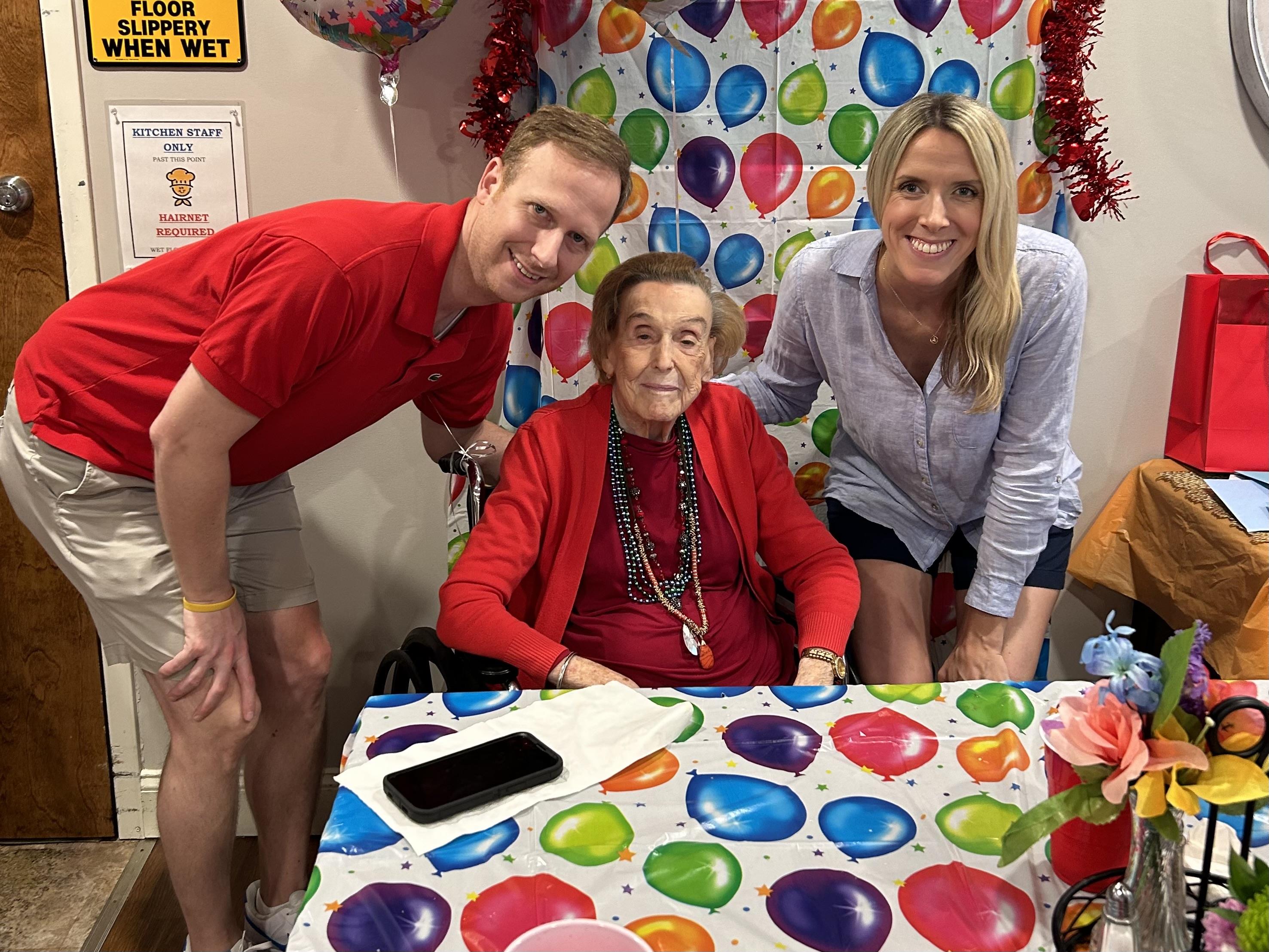 A cheerful family gathers around a decorated table with an elderly woman in red.