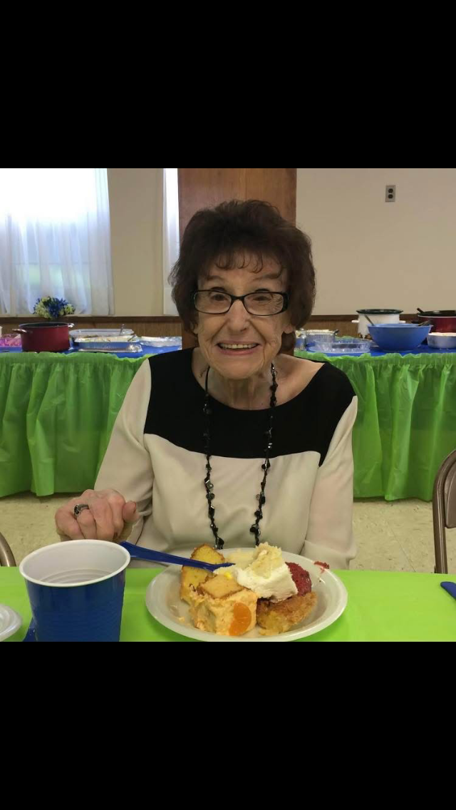 An elderly woman enjoys a variety of desserts at a festive community event.