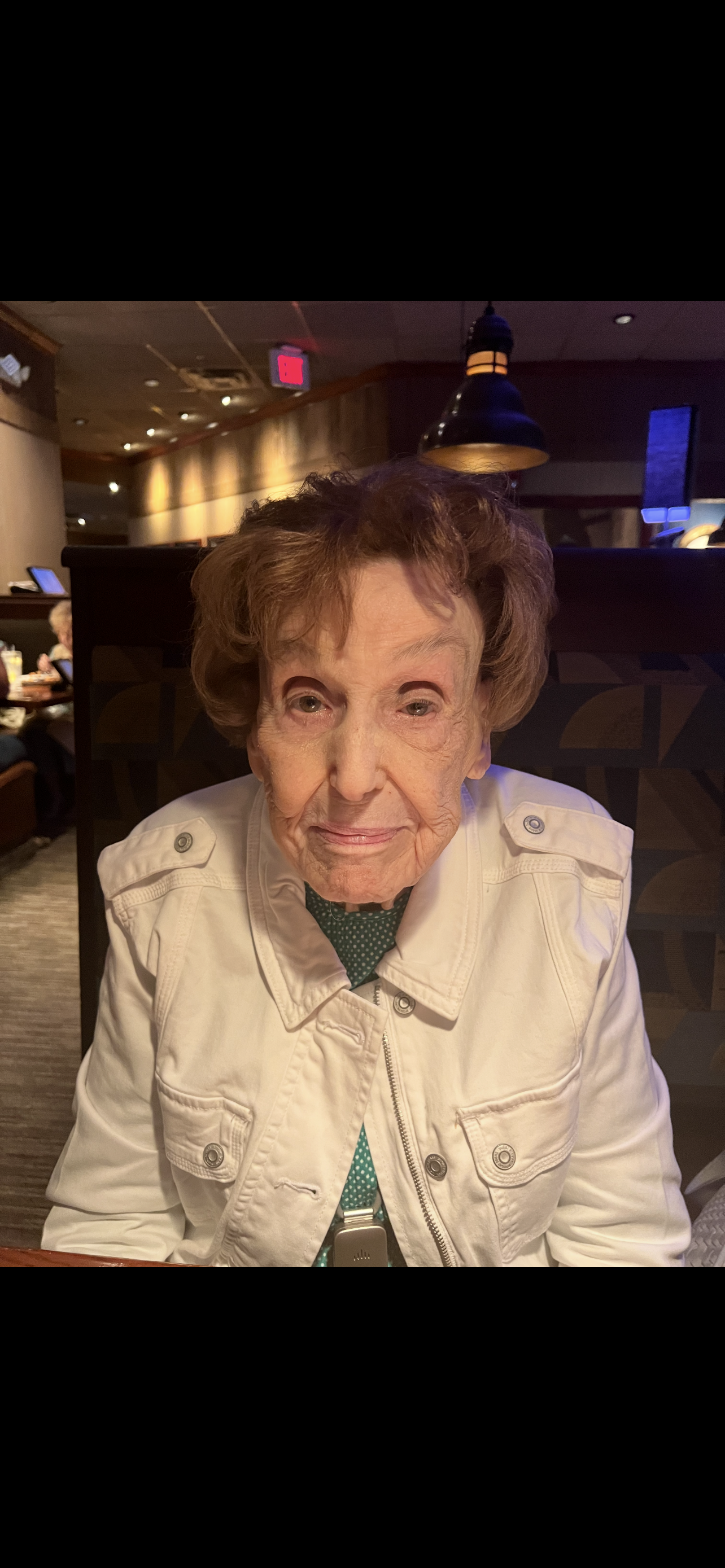 A woman in a white jacket smiles warmly while enjoying time with others at a restaurant.