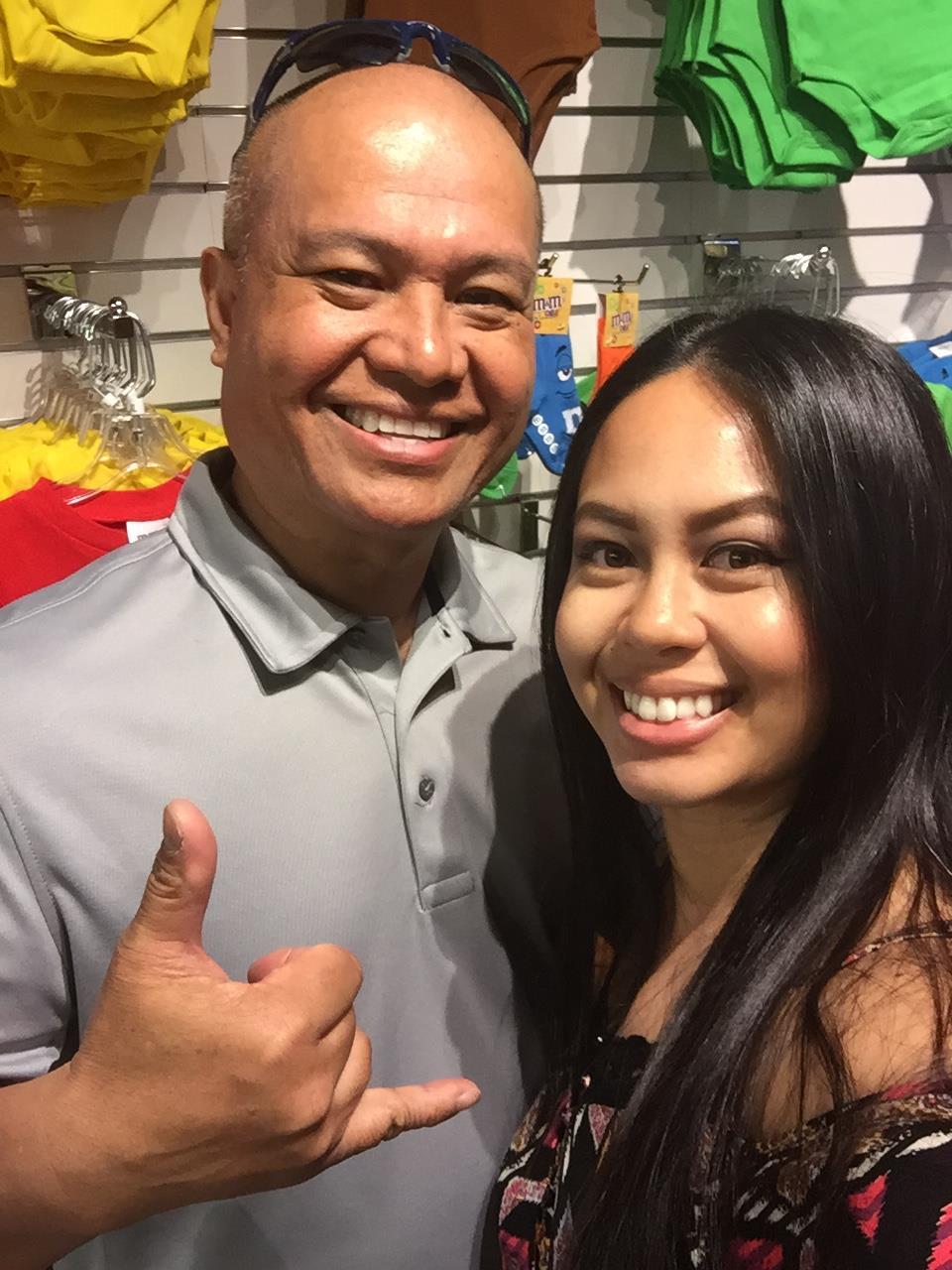 Two individuals stand together, smiling and making fun gestures in a busy clothing store.