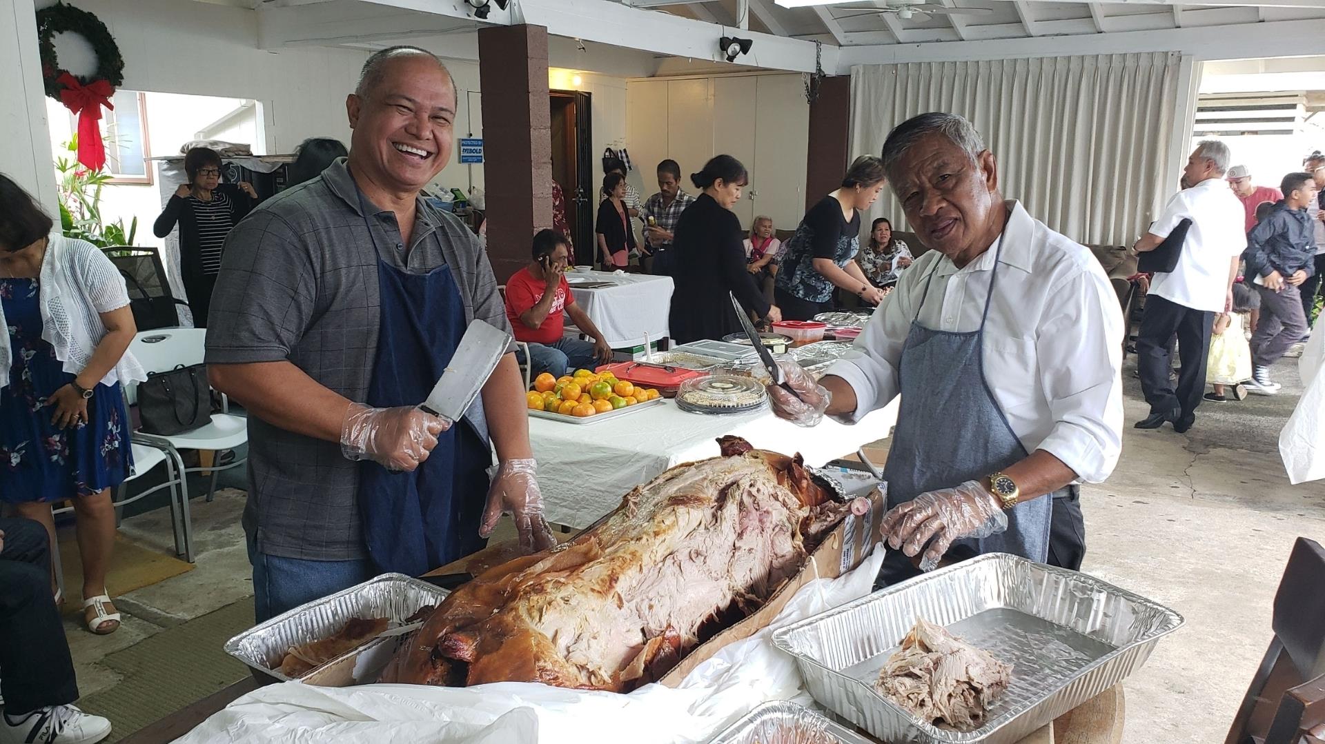 Two chefs expertly carve a roasted pig at a lively community event with joyful attendees.
