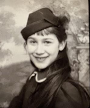 A young girl poses with a charming smile, wearing a fashionable hat in an old photograph.