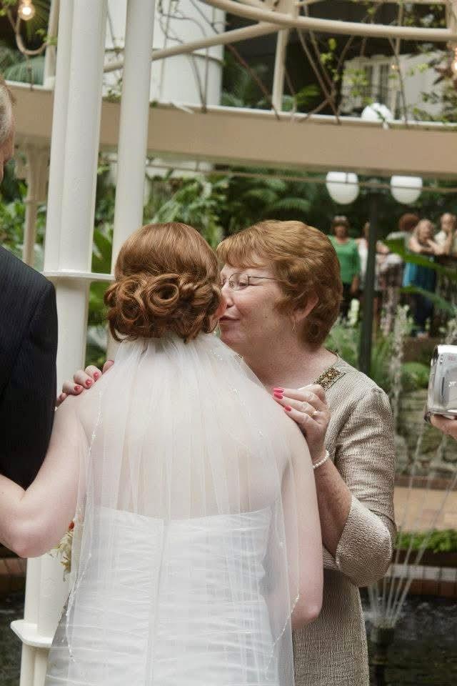Emotional interaction between mother and bride in a beautiful garden setting filled with guests.