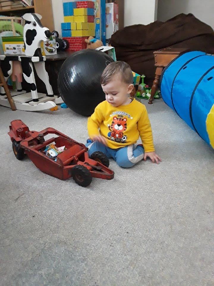 A child sits on the floor, engaged with a red toy car in a vibrant playroom filled with toys.