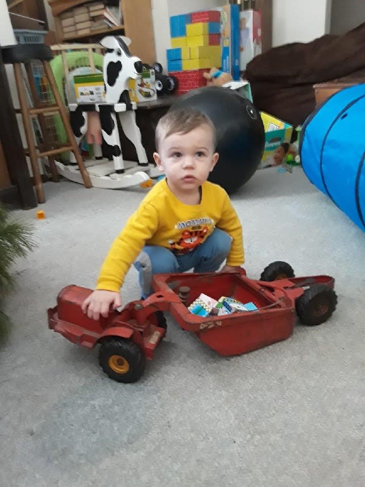 A young child interacts with a bright red toy tractor, surrounded by playful decorations.