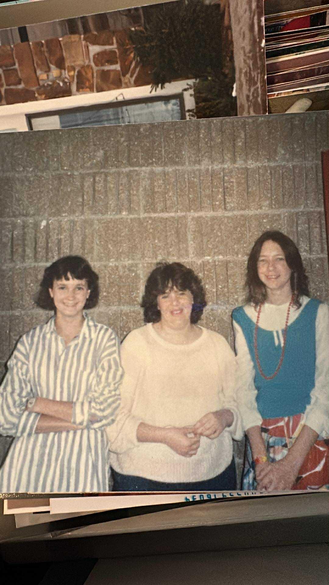 Three friends stand together, smiling warmly at the camera in a casual setting.