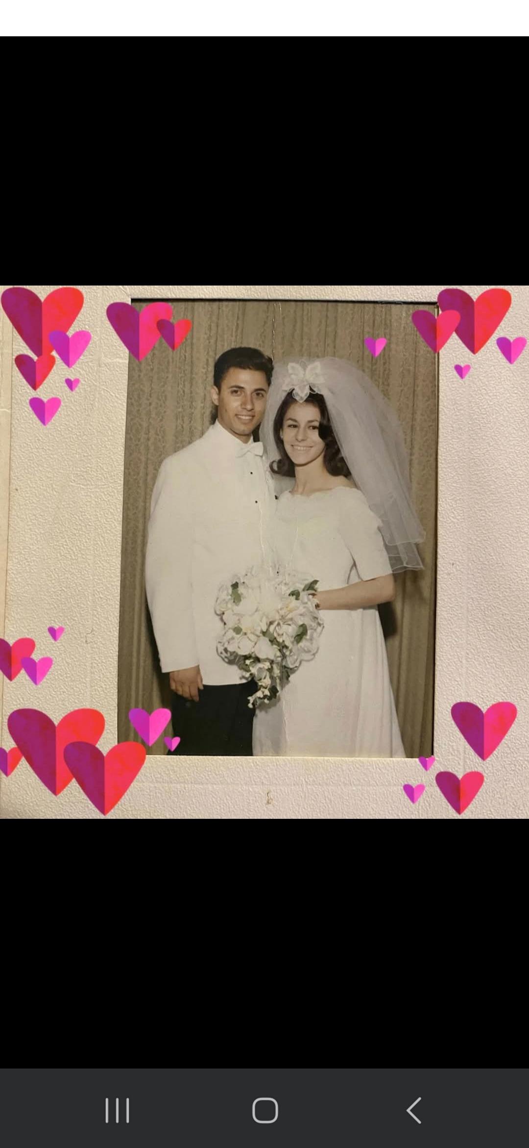 A couple dressed in formal wedding attire poses joyfully with a bouquet and a heartfelt backdrop.