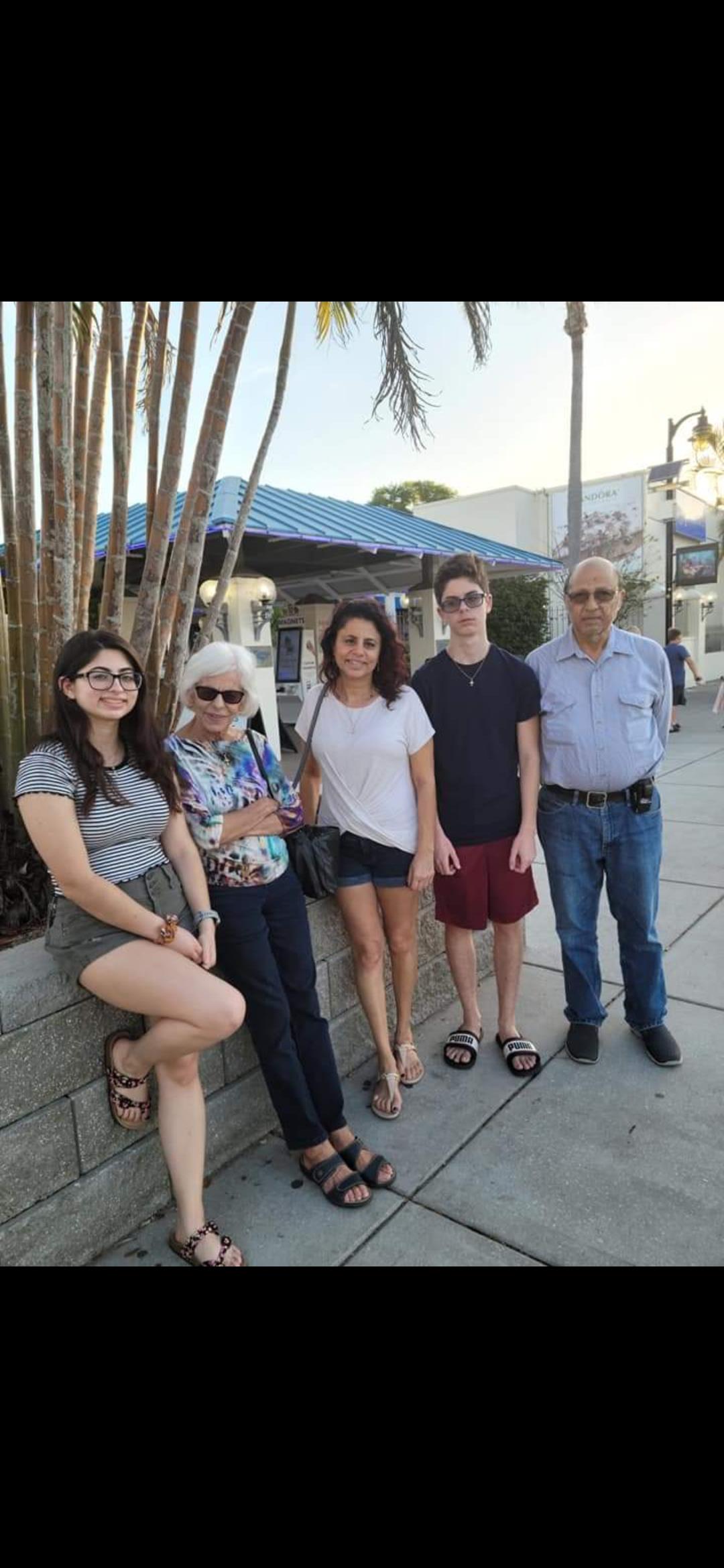 A group of five stands relaxed against a stone wall on a sunny street, enjoying their time together.