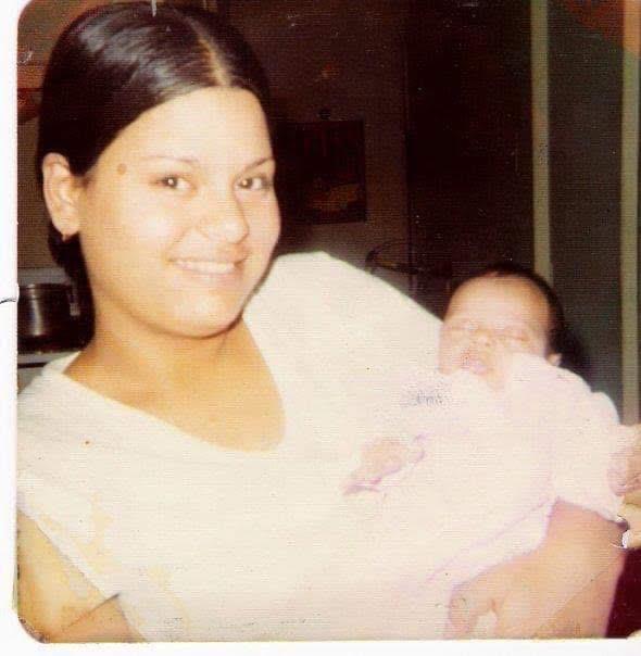 A woman smiles lovingly while cradling her infant in a comfortable home environment.