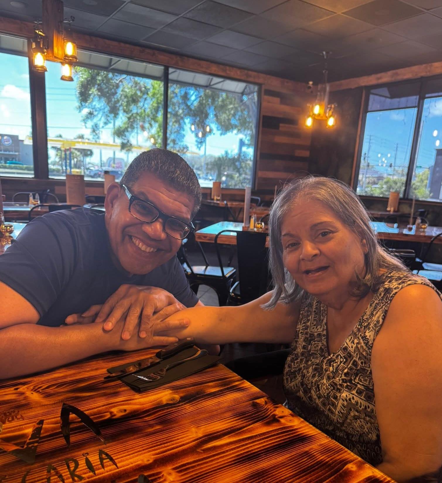 A man and a woman are smiling and holding hands at a restaurant table, enjoying their time.
