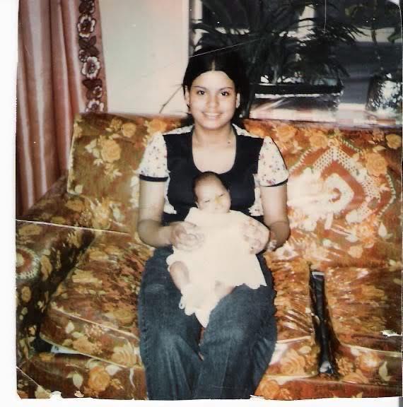 A mother smiles while cradling her newborn baby on a colorful couch in a cozy living room.